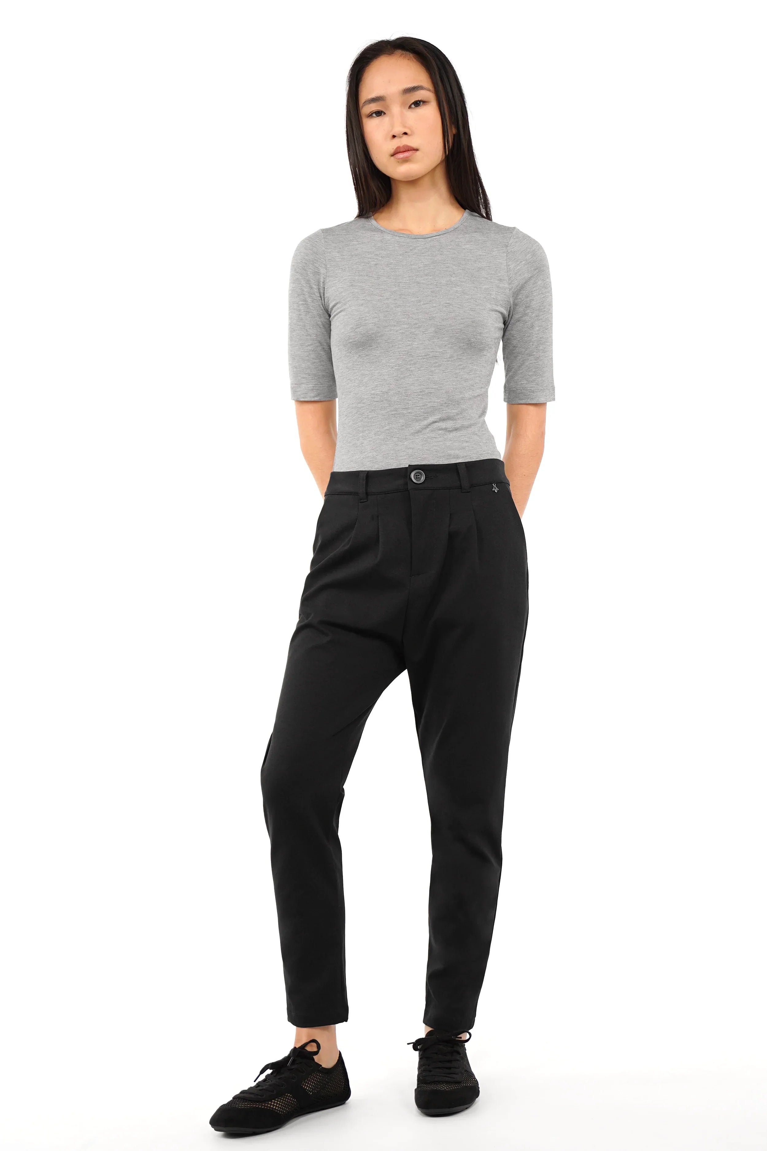 Woman wearing black HEELENA tapered pants with a fitted waist and slim legs paired with a gray fitted top and black sneakers