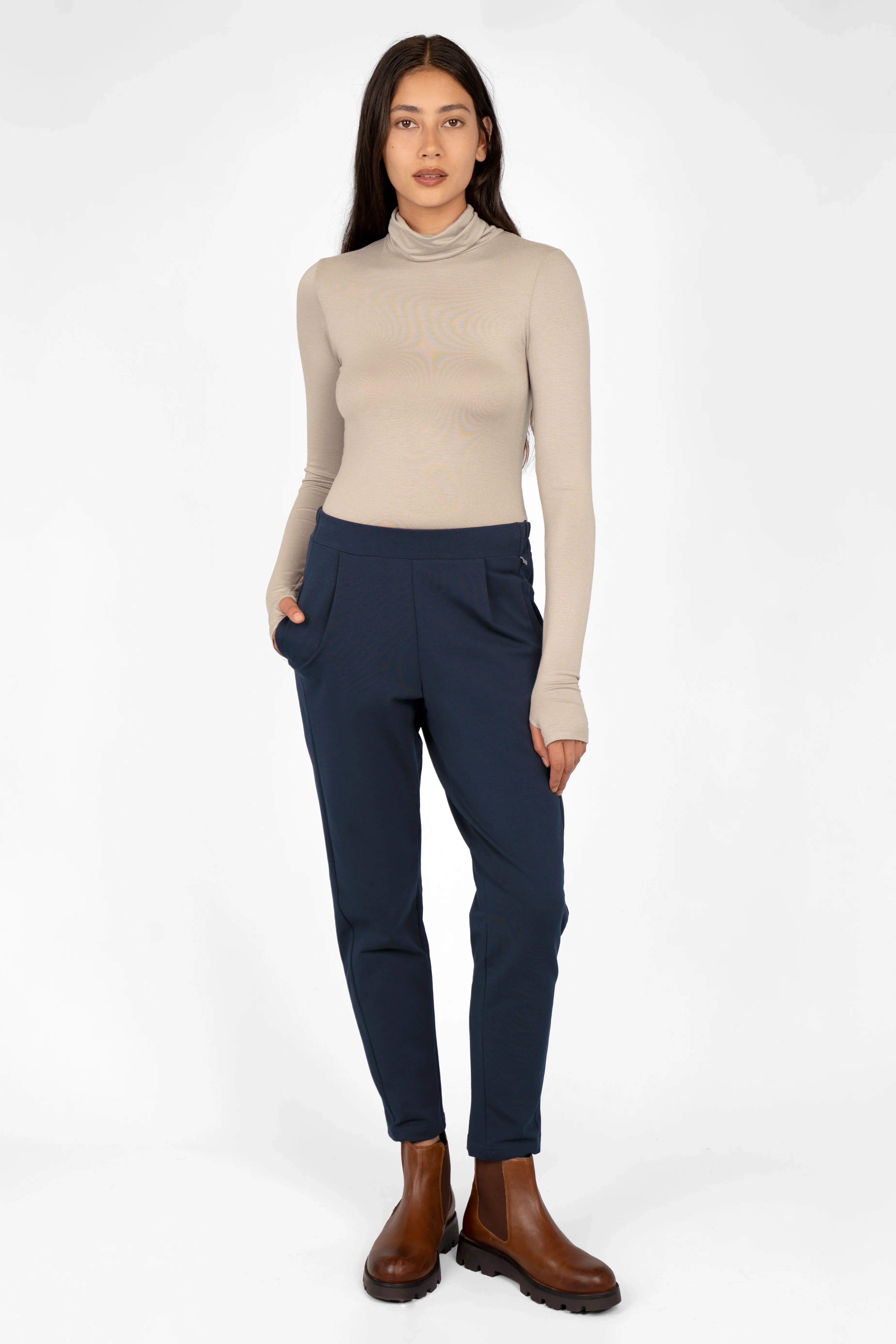 Damen trägt HILLA.K Jerseyhose in Dunkelblau mit regular fit, mittelhohem Bund und schmal zulaufendem Bein kombiniert mit beigem Rollkragenpullover und braunen Stiefeln.