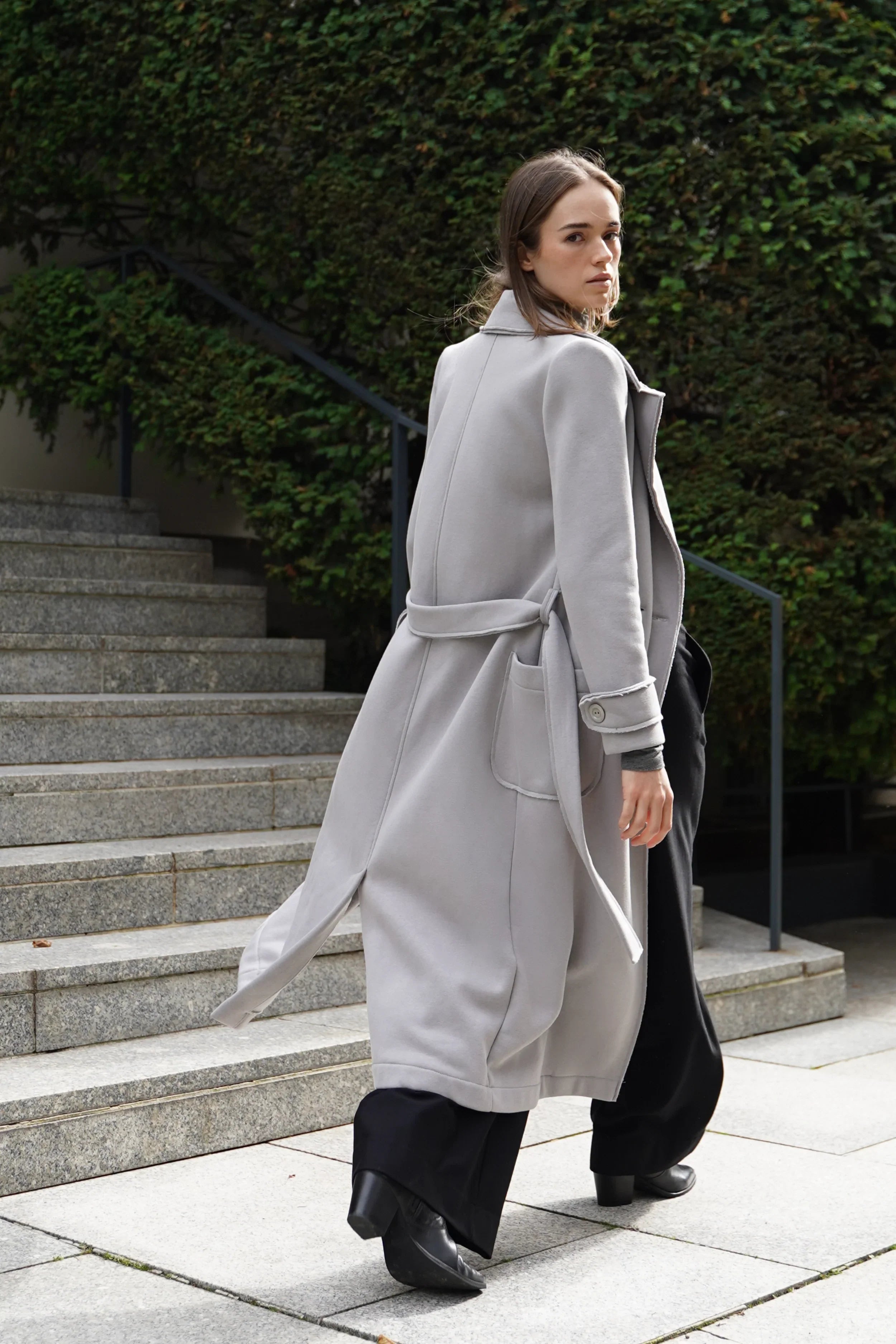 Frau trägt hellgrauen INGE Sweatmantel mit Bindegürtel und Rückenlänge 124 cm draußen auf Treppe