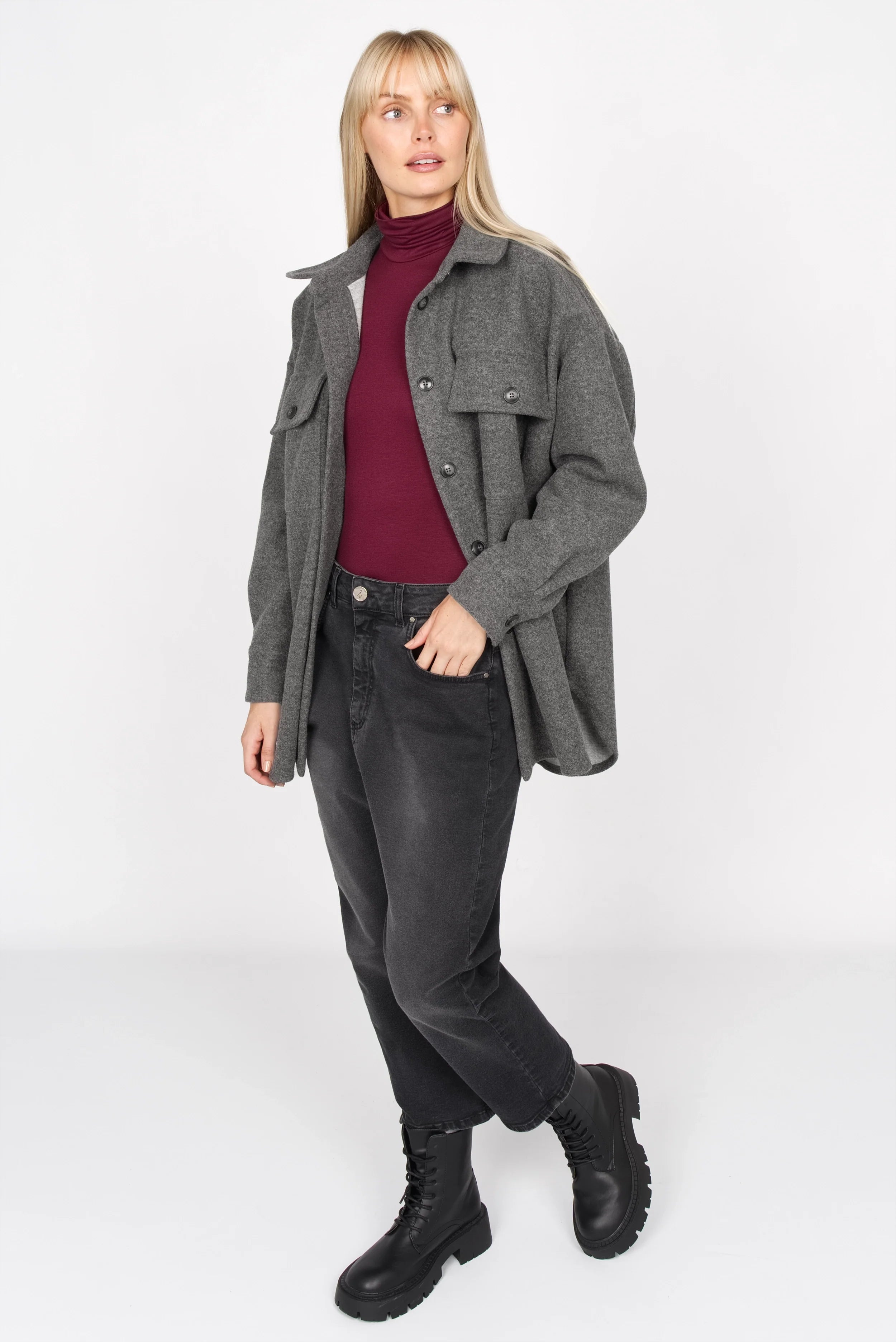 Frau trägt INNEKA Longsleeve mit Rollkragen in Burgunderrot und graue Jacke, schwarze Jeans und Stiefel