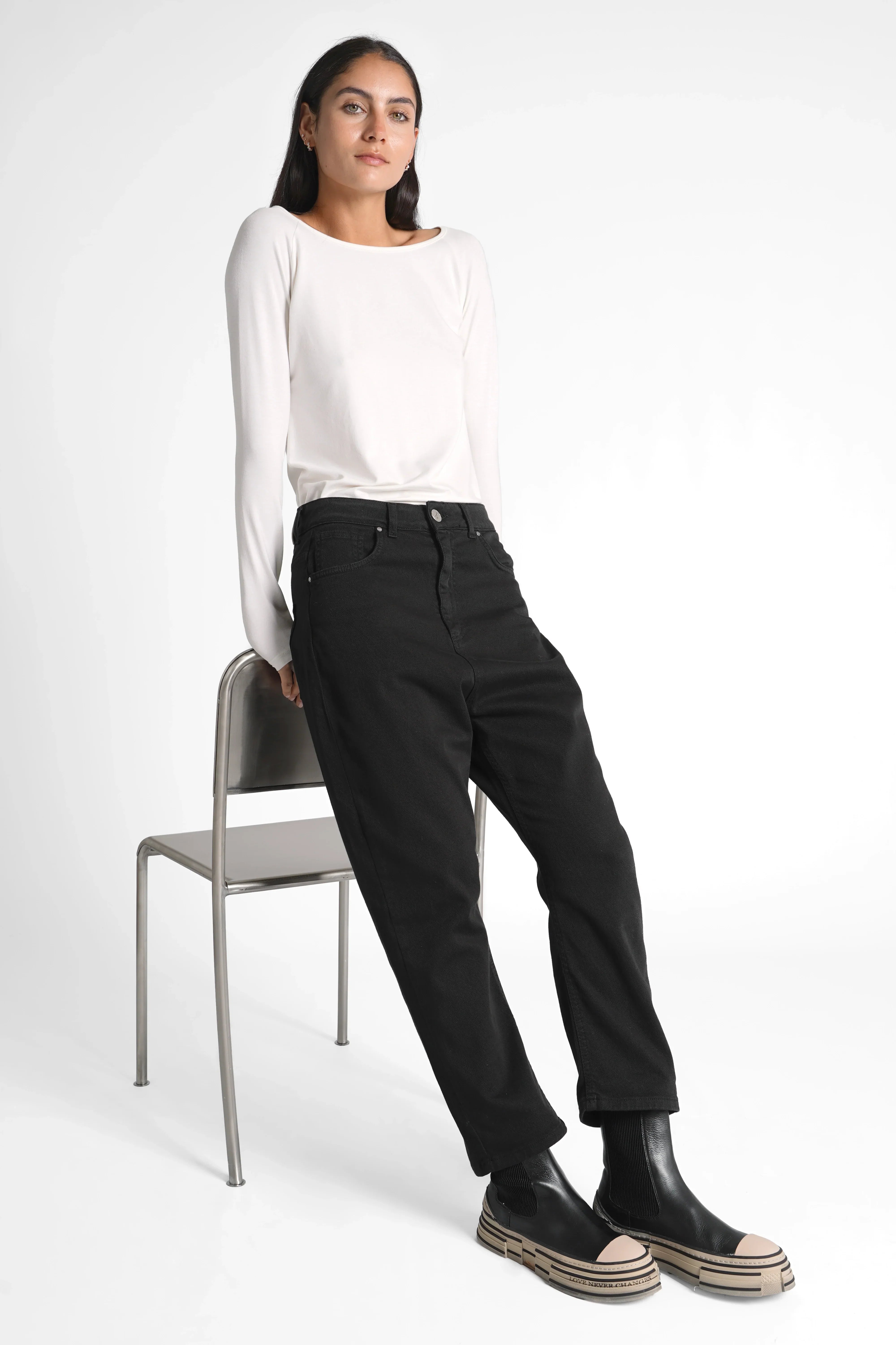 Woman wearing black relaxed fit baggy jeans sitting on a chair with a white long-sleeve top and black boots