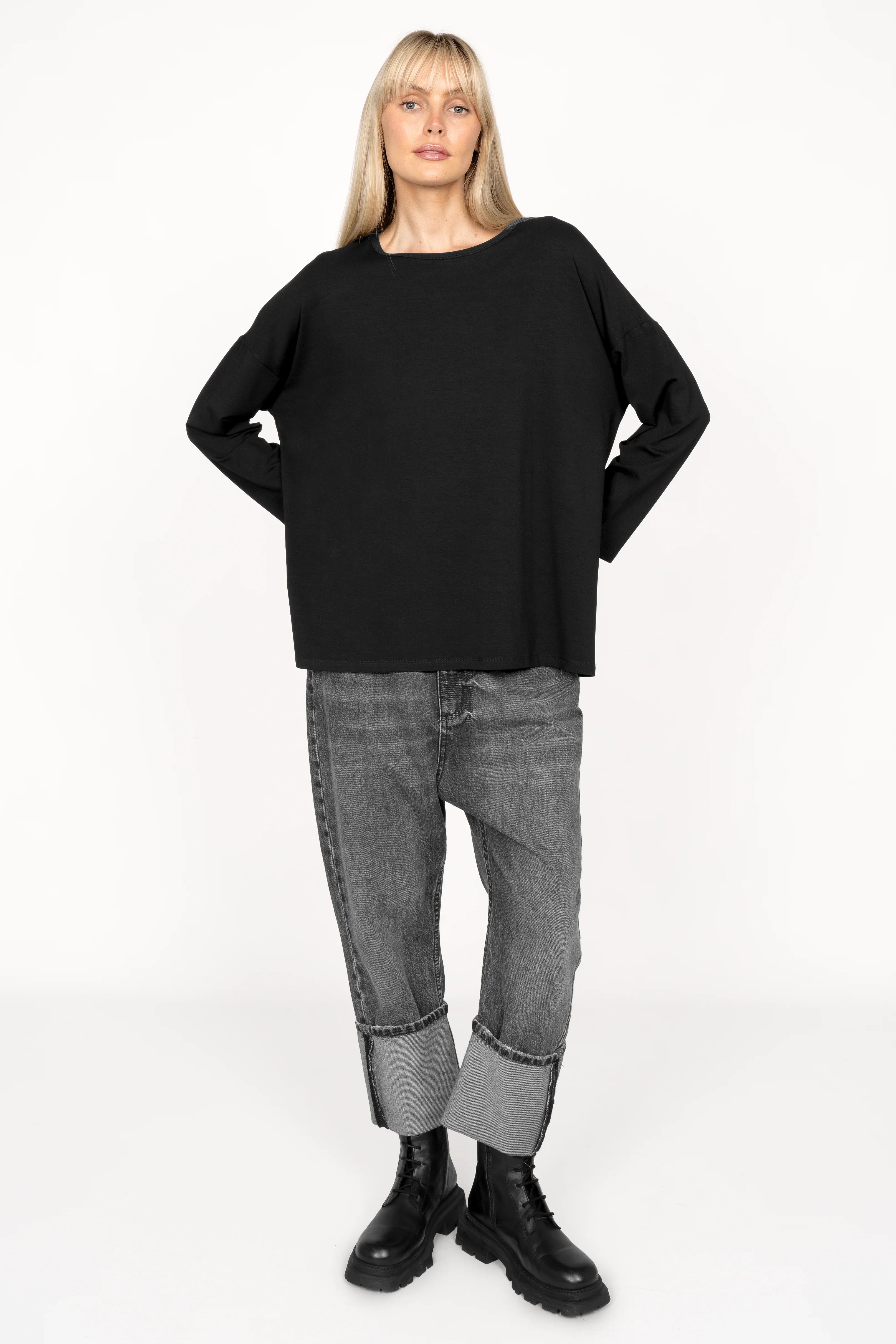 Woman wearing black JENEN Oversized Longsleeve with round neckline and dropped shoulders paired with cuffed gray jeans and black boots.