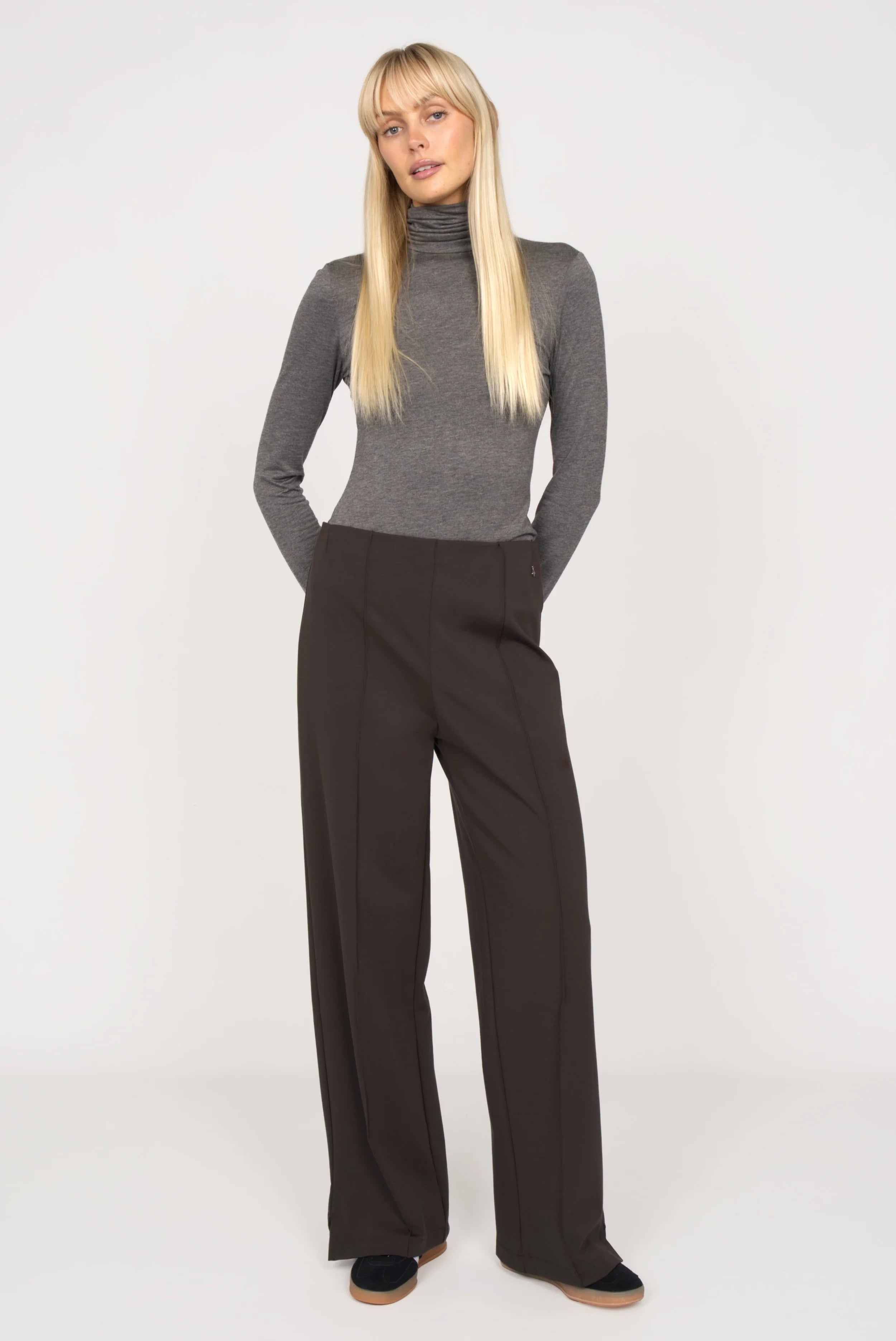 Woman wearing KANDANEA Gerade Hose in dark color with front pintucks and elastic waistband, paired with gray turtleneck sweater.