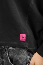Black KERY Cropped Sweater with oversized fit, U-boat neckline, and pink STUDIO logo patch on hem.