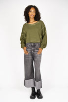 Woman wearing oversized olive green KERY Cropped Sweater with U-boat neckline and cold-washed cotton fabric paired with cuffed wide-leg jeans and black boots.