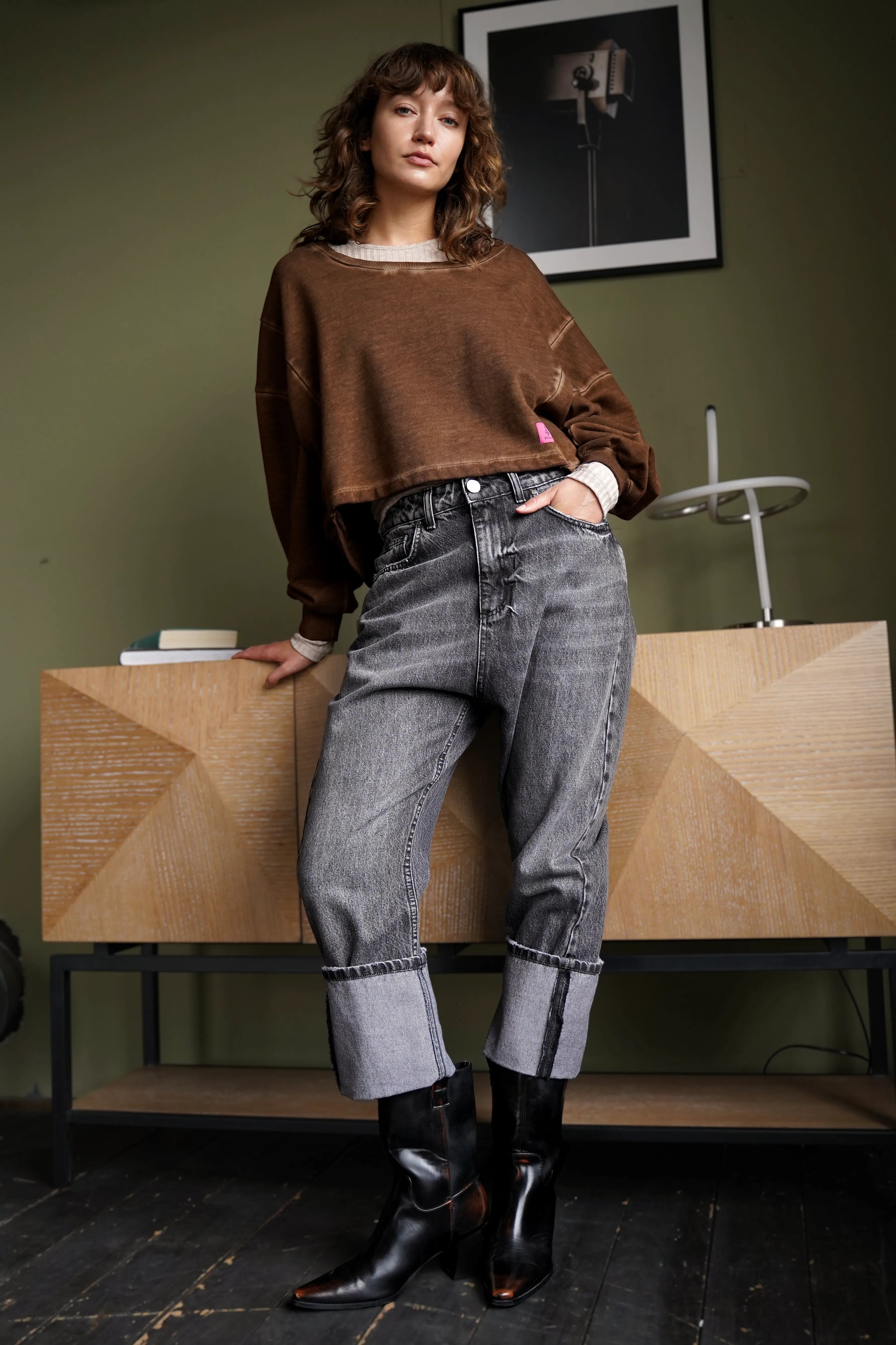 Frau trägt lässigen braunen KERY Cropped Sweater mit oversized Passform und U-Boot-Ausschnitt kombiniert mit grauen Jeans und schwarzen Stiefeln