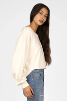 Damen trägt cremefarbenen KERY Cropped Sweater mit U-Boot-Ausschnitt, oversized Passform und überschnittenen Schultern kombiniert mit Jeans