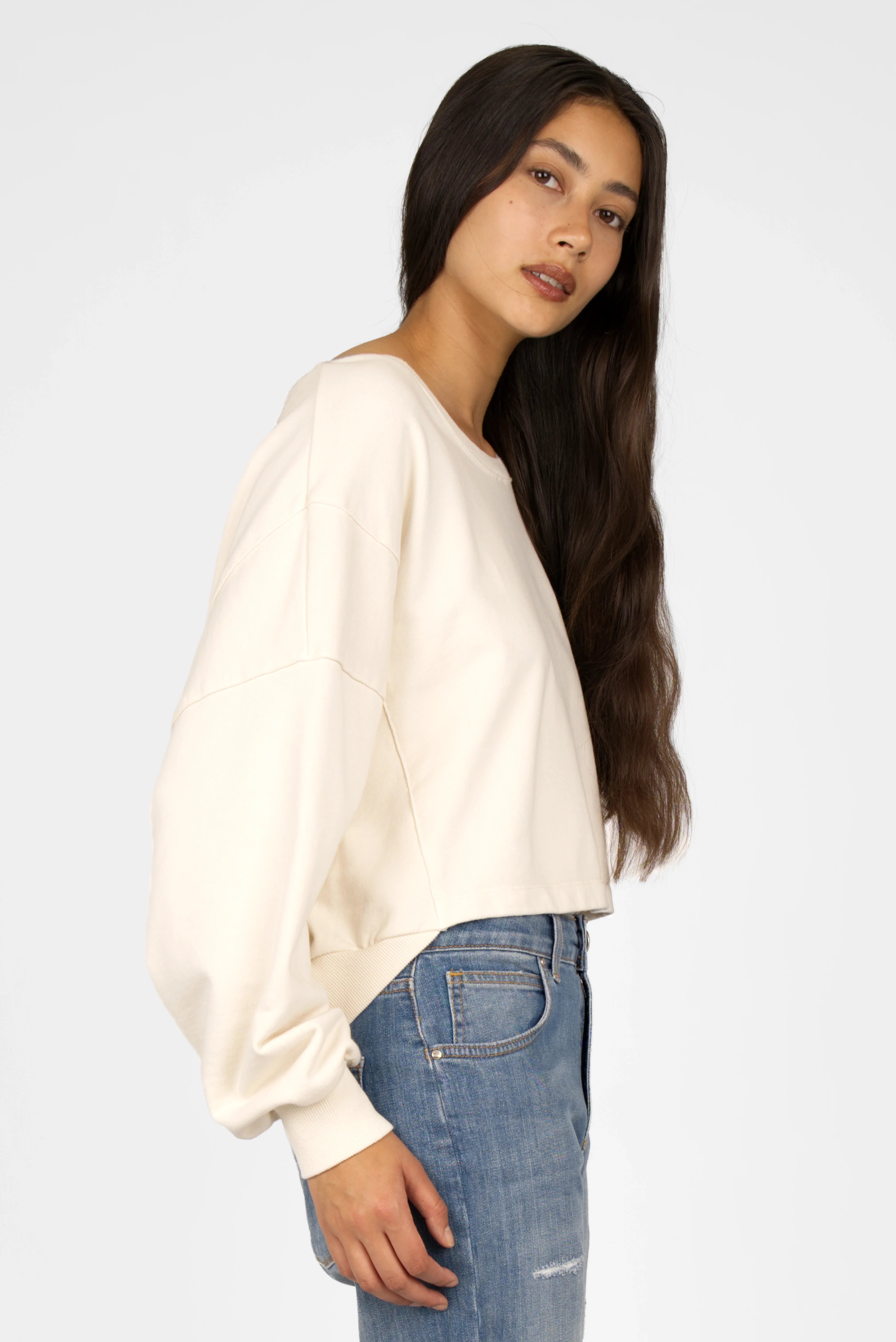 Damen trägt cremefarbenen KERY Cropped Sweater mit U-Boot-Ausschnitt, oversized Passform und überschnittenen Schultern kombiniert mit Jeans