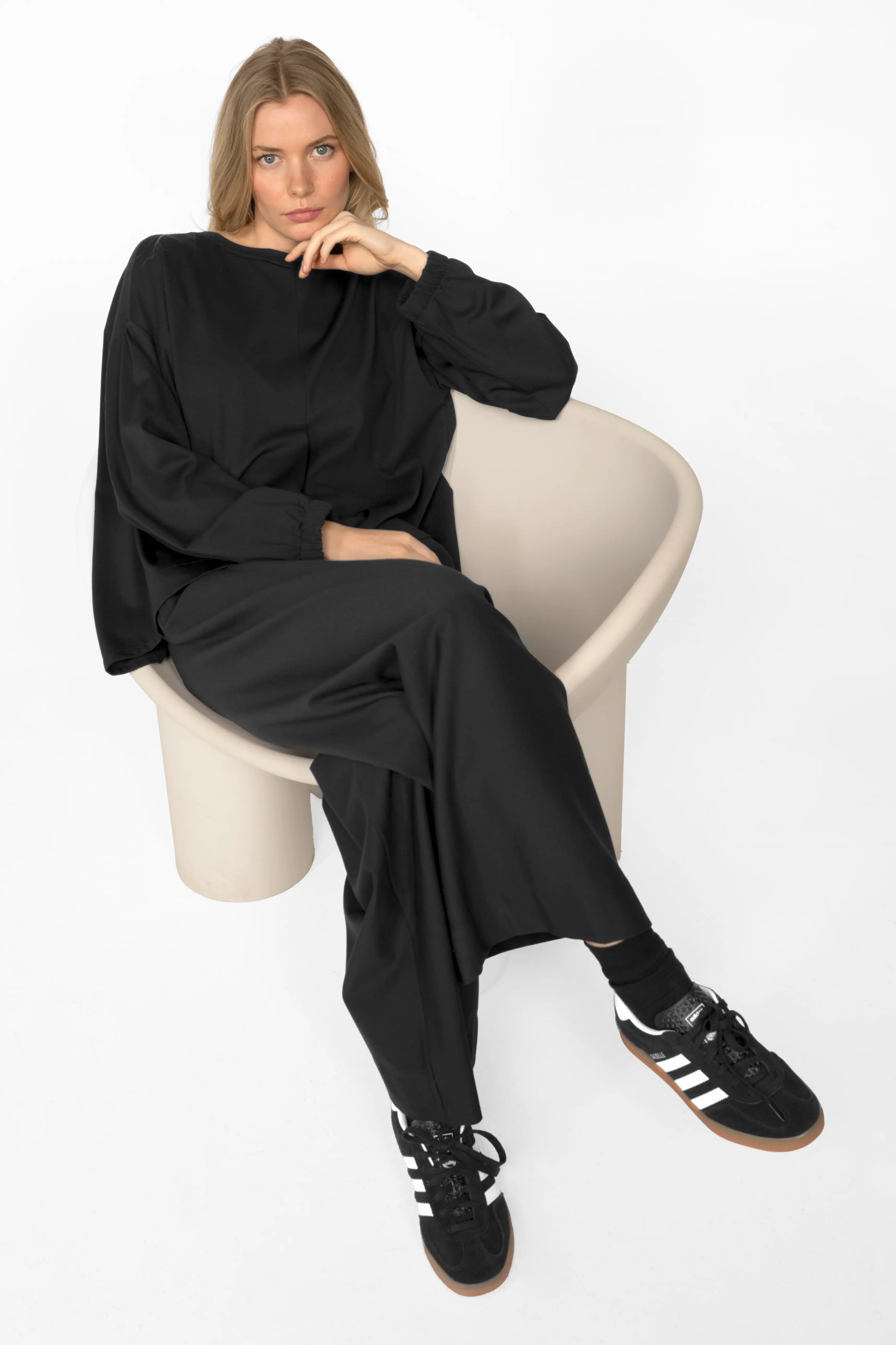 Frau trägt schwarze KLARA.K Wide Leg Pants mit weitem Bein, elastischem Bund und seitlichen Eingrifftaschen, kombiniert mit schwarzem Oberteil und Sneakers