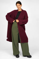 Frau trägt KLARA.K Wide Leg Pants in Olivegrün mit elastischem Bund und seitlichen Taschen kombiniert mit langem bordeauxrotem Strickcardigan