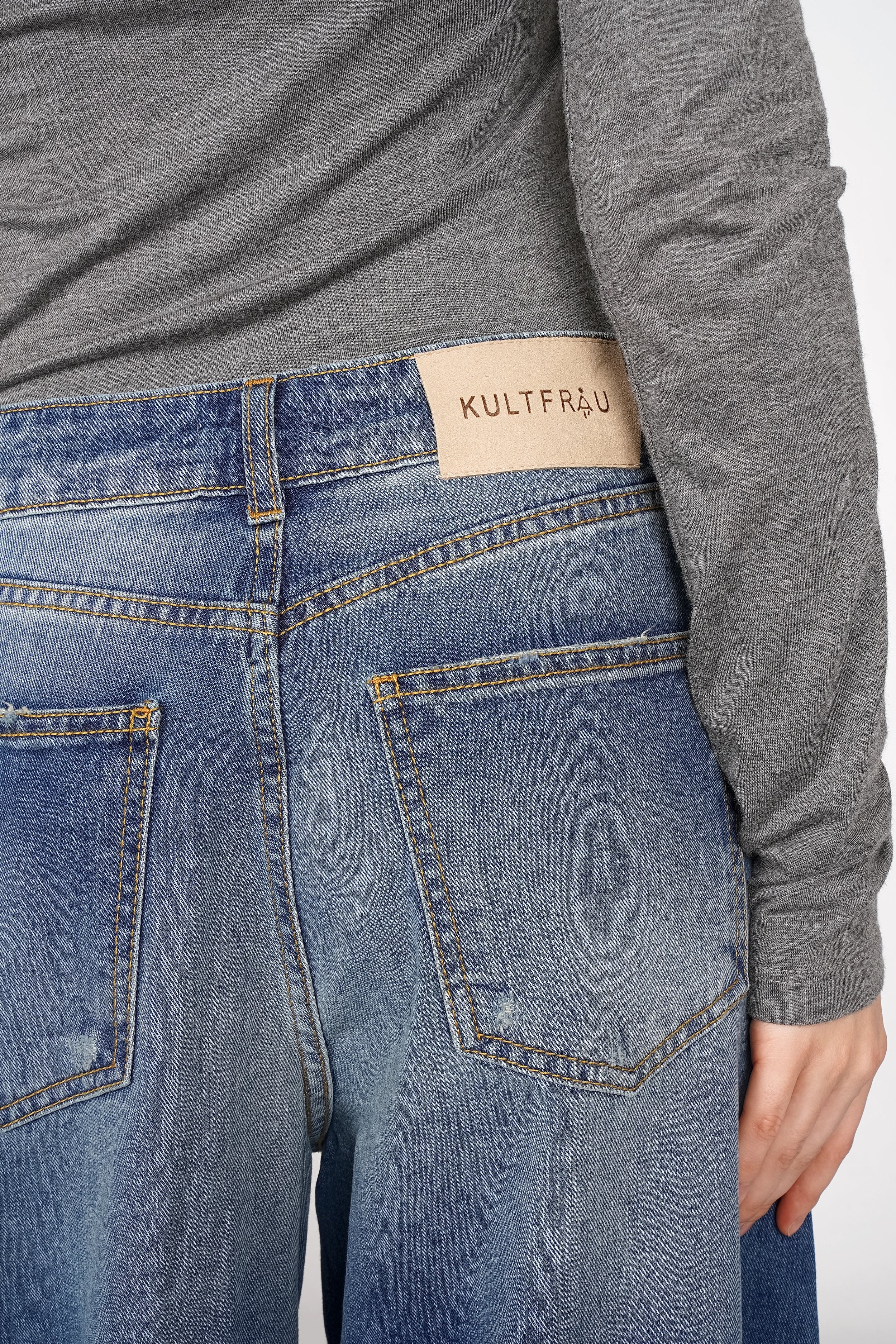 Back view of relaxed fit wide barrel jeans with faded denim and raw-cut hem