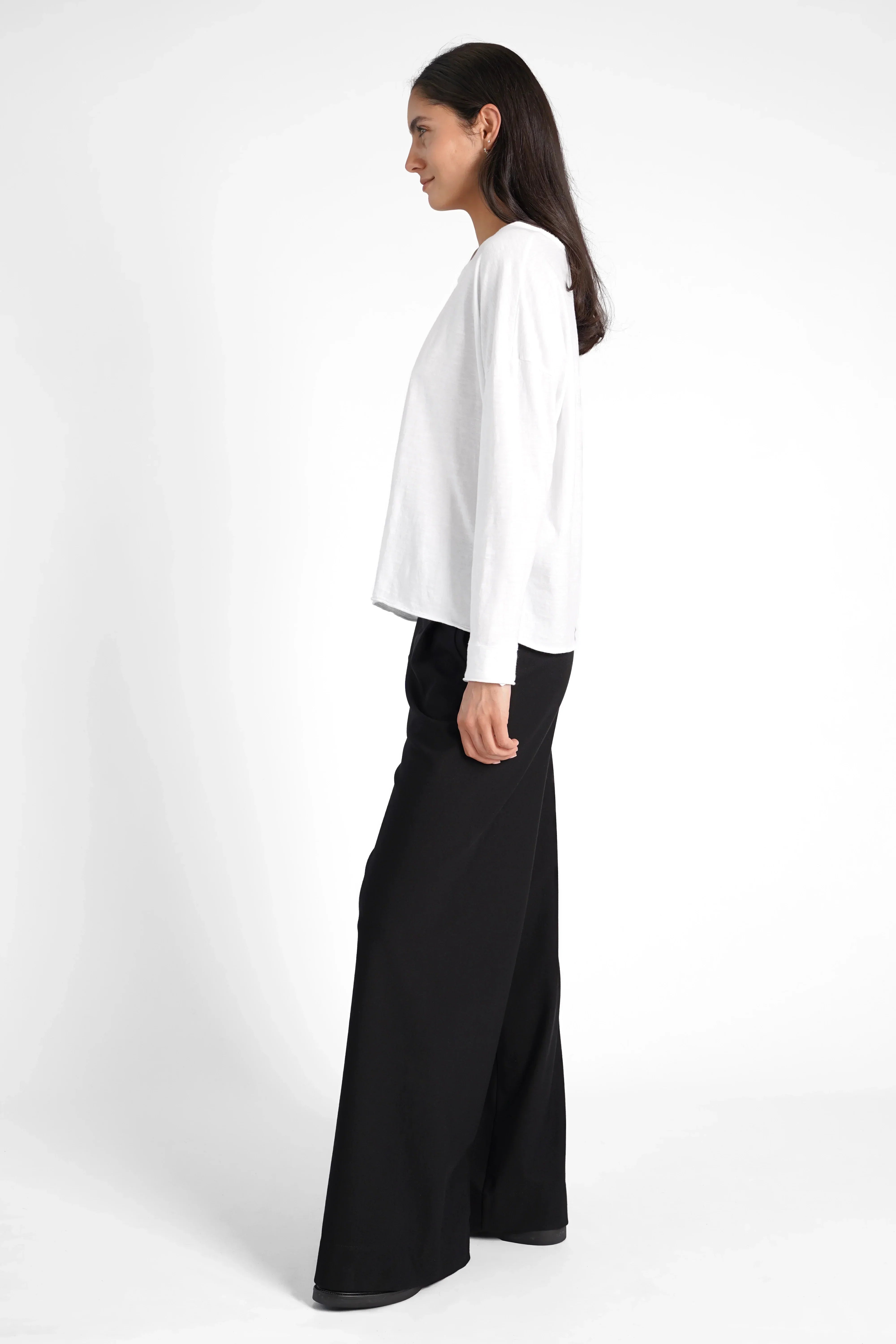 Woman wearing white LARXA Longsleeve with round neckline and black wide-leg pants side view