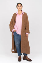 Woman wearing LEA.K Loose Fit pink cotton poplin blouse with wide cuffs and chest pockets layered under a long brown knitted cardigan and blue jeans