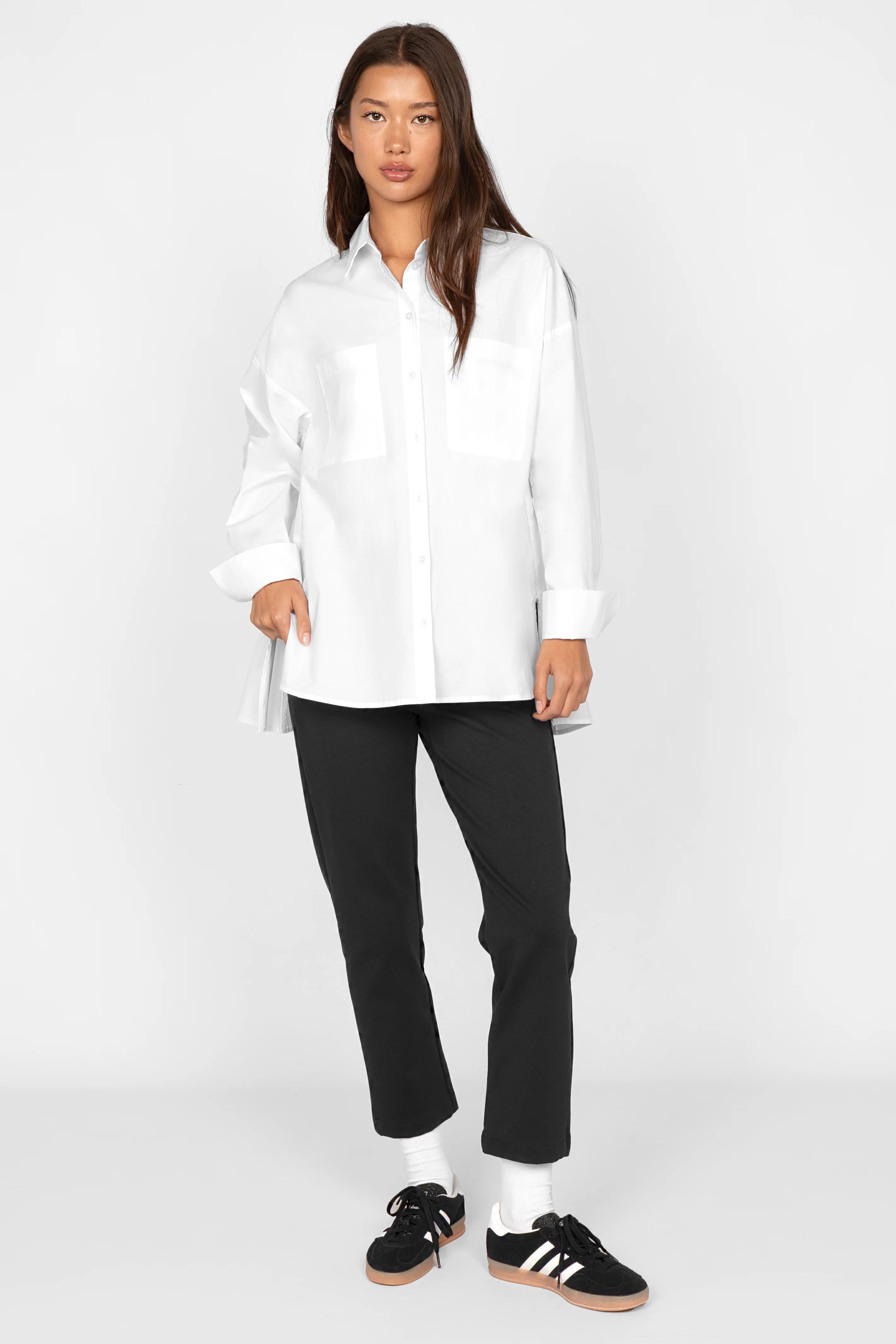 Woman wearing white LEA.K Loose Fit cotton poplin blouse with chest pockets and buttoned cuffs paired with black pants and sneakers