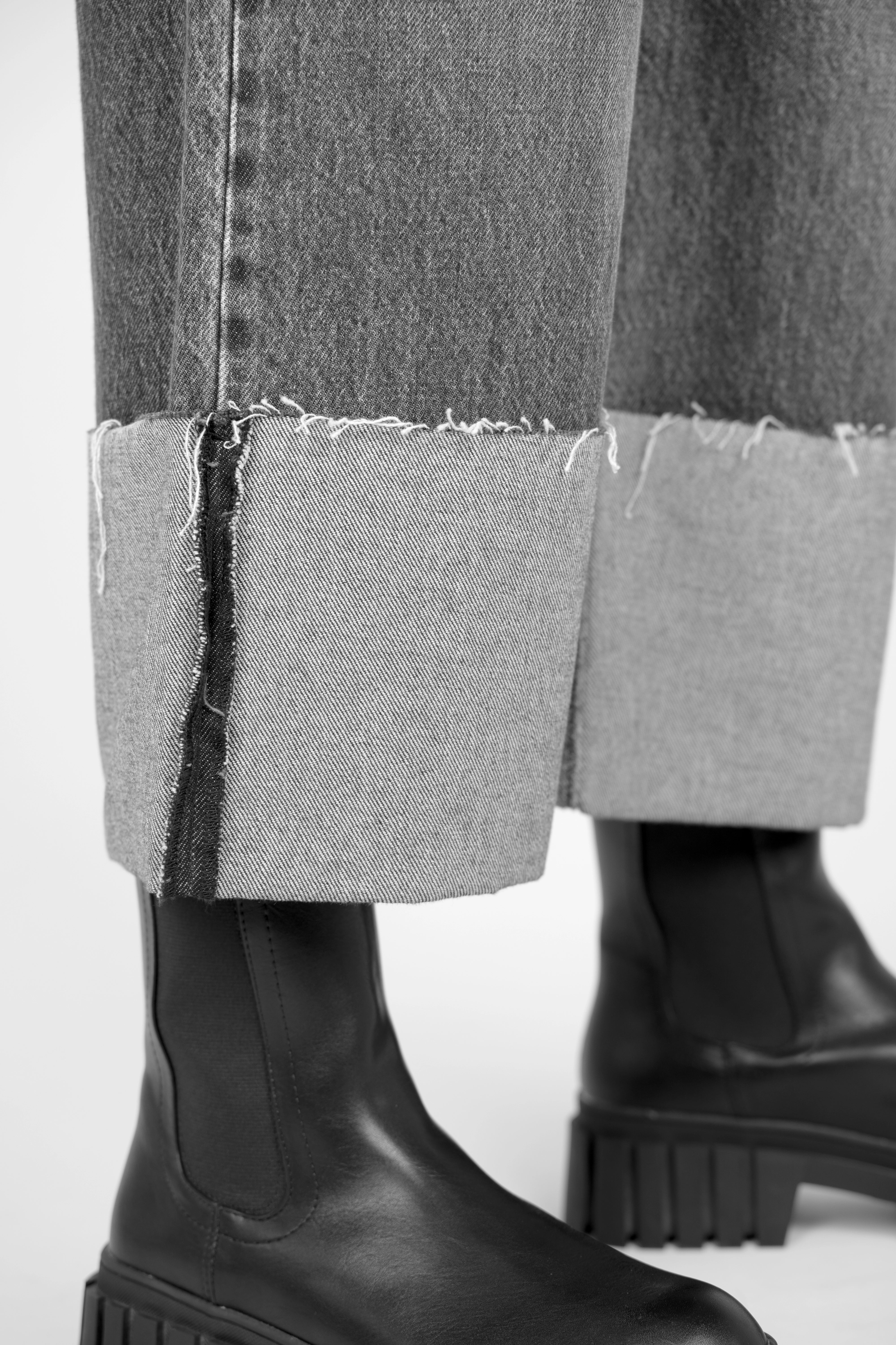 Close-up of LIAME Cropped Jeans with raw-cut cuff and black chunky boots showing relaxed fit and whisker effect