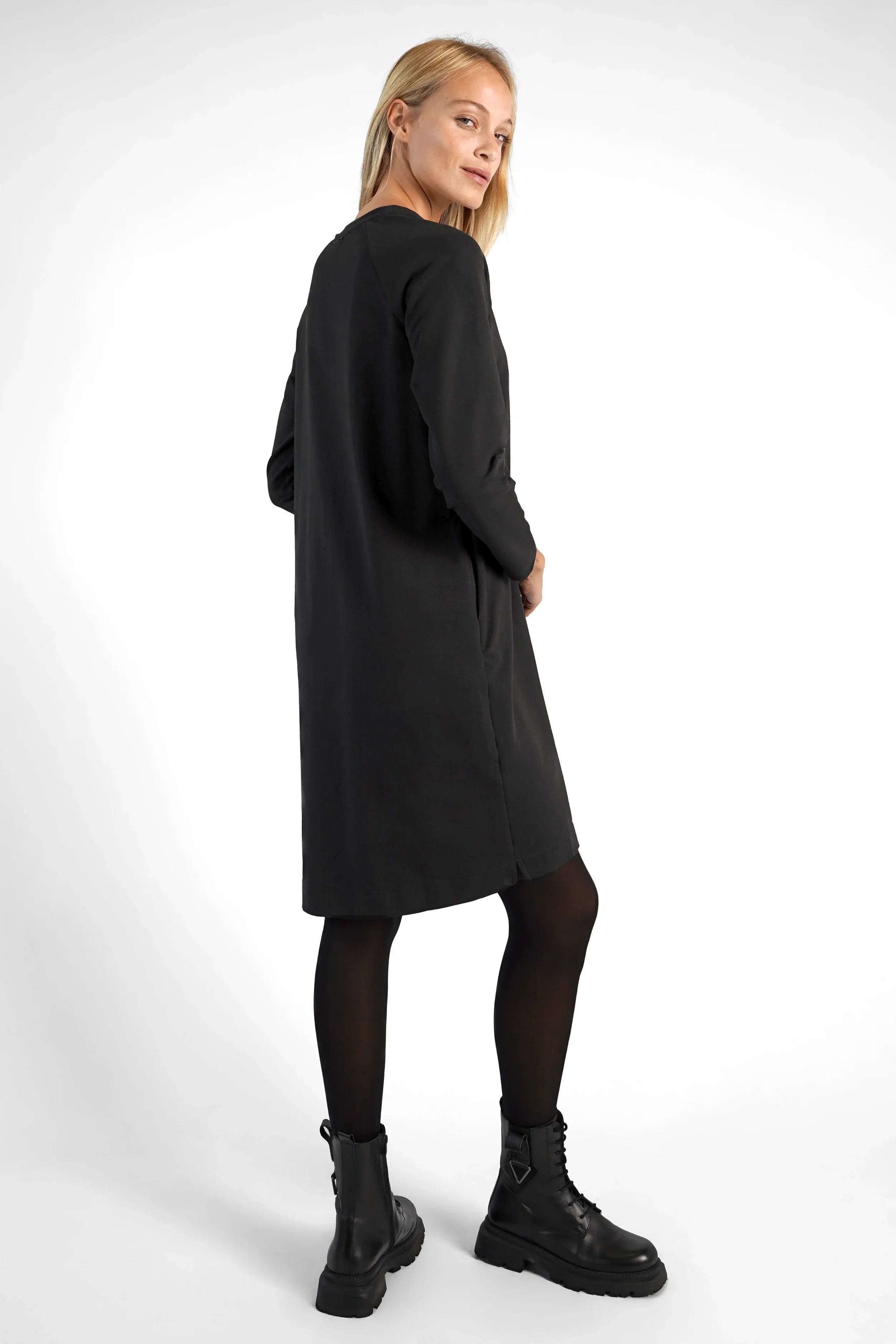 Frau trägt schwarzes LIZ Sweatkleid mit Rundhalsausschnitt, Seitentaschen und leicht abgerundetem Saum.