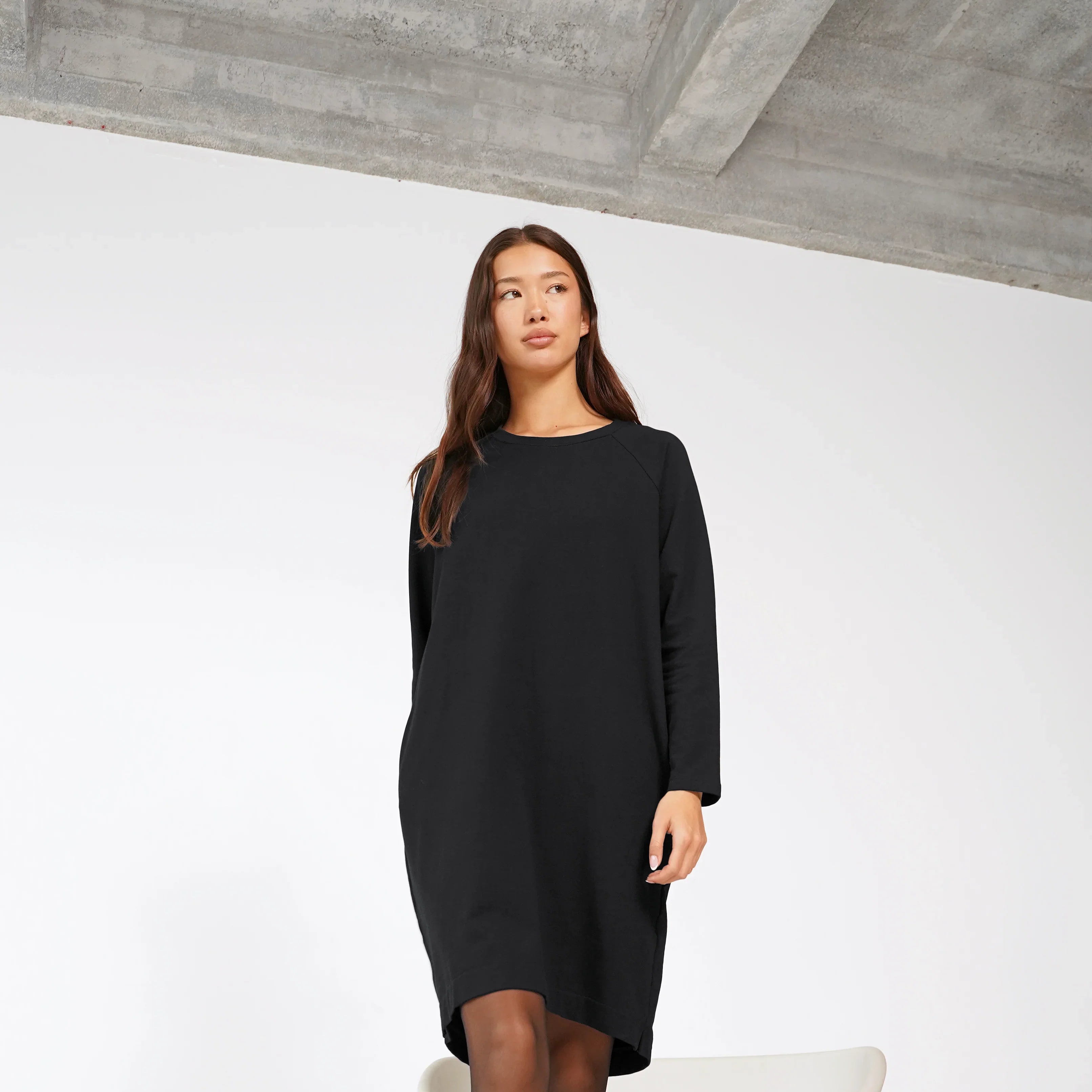 Frau trägt schwarzes LIZ Sweatkleid mit Rundhalsausschnitt und Seitentaschen, relaxed Schnitt, hinten länger, Baumwolle, knieumspielend