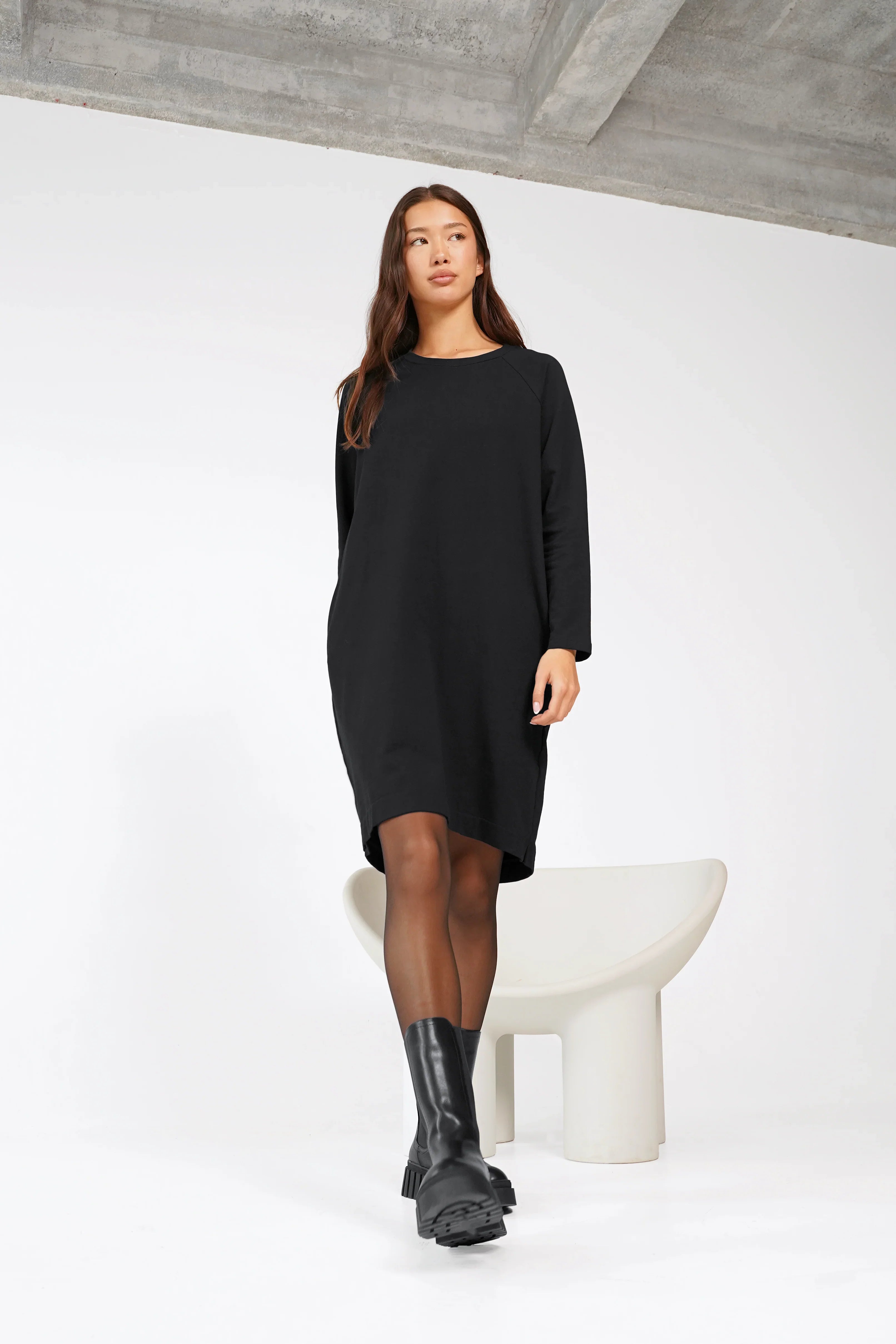 Frau trägt schwarzes LIZ Sweatkleid mit Rundhalsausschnitt und Seitentaschen, relaxed Schnitt, hinten länger, Baumwolle, knieumspielend