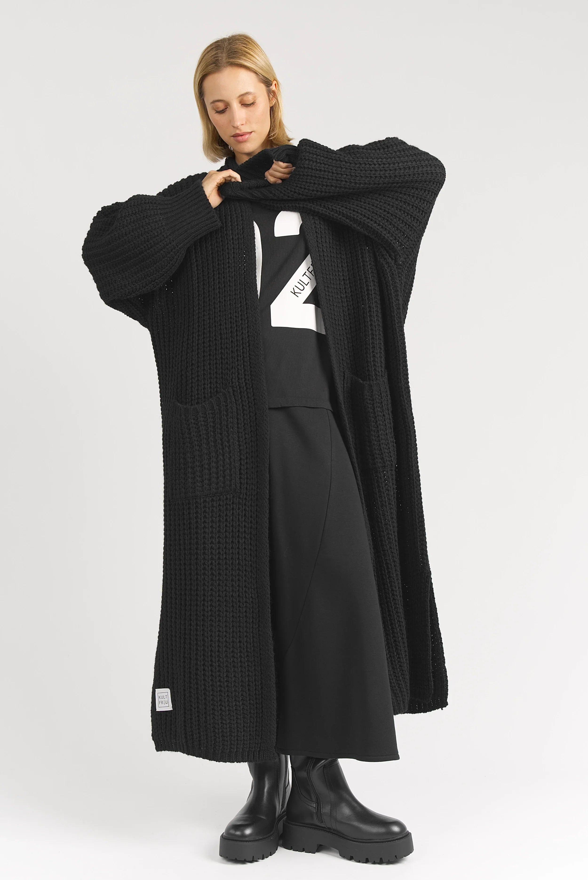 Frau trägt schwarzen LOLA Strickcardigan oversized offen mit aufgesetzten Taschen und lockerem Schnitt