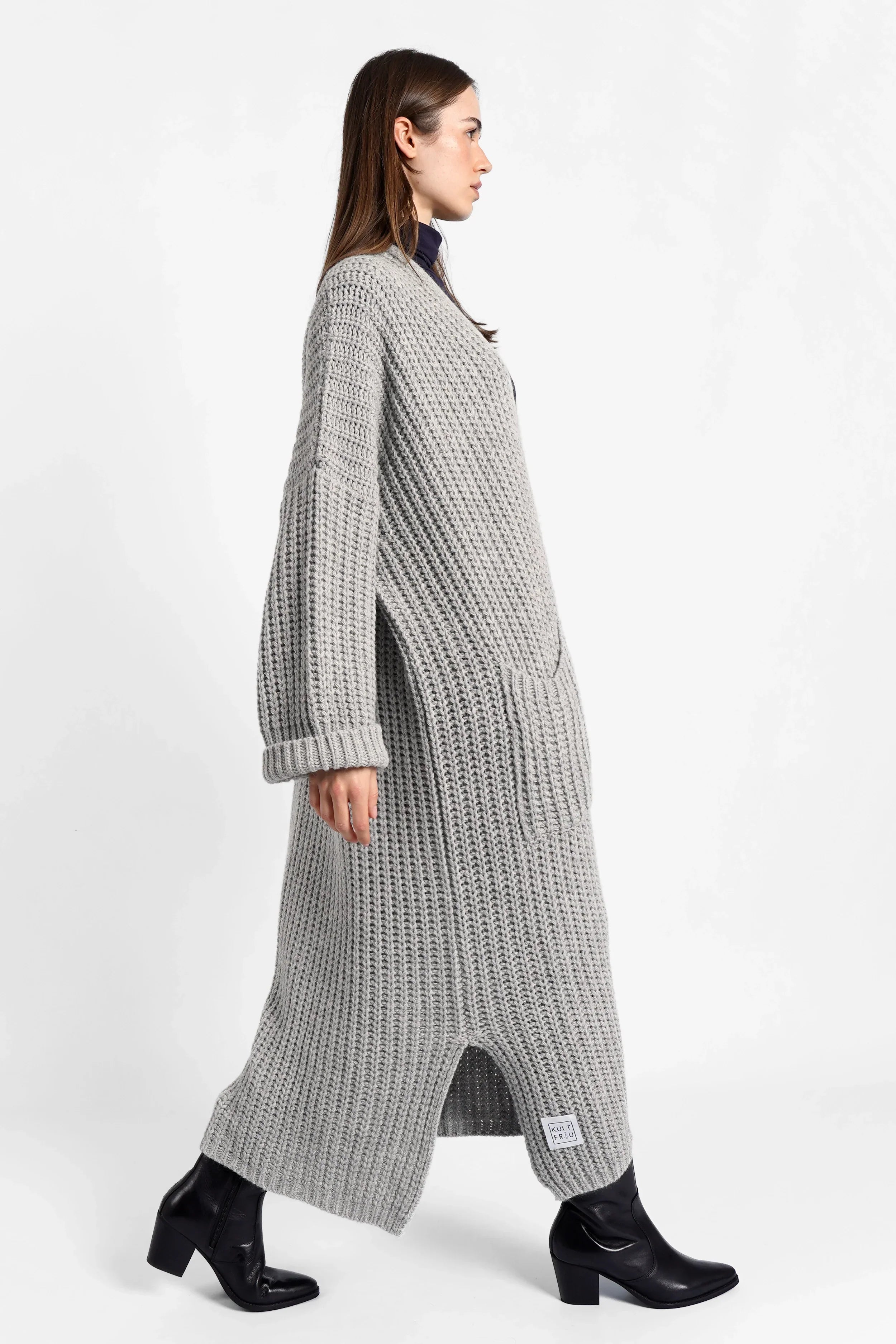 Woman wearing grey oversized LOLA Strickcardigan knit cardigan with rolled sleeves and patch pockets walking against white background