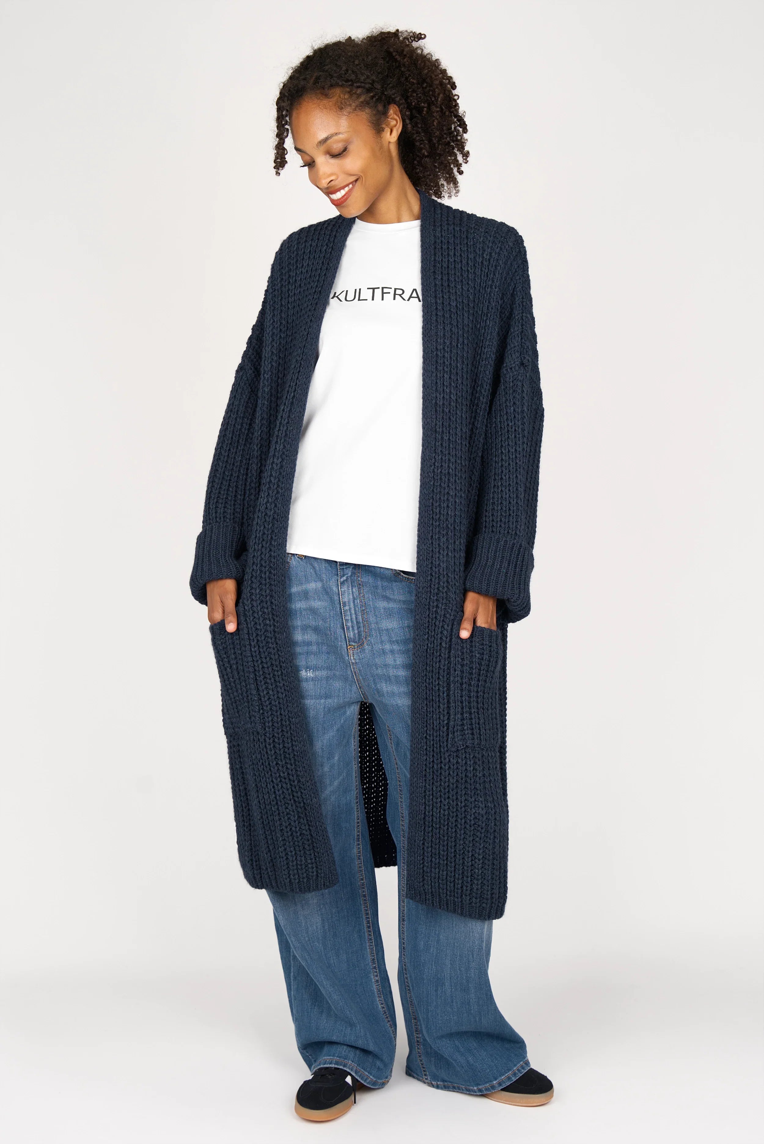 Frau trägt oversized Strickcardigan LOLLYTA in dunkelblau offen mit umgeschlagenen Ärmeln und aufgesetzten Taschen