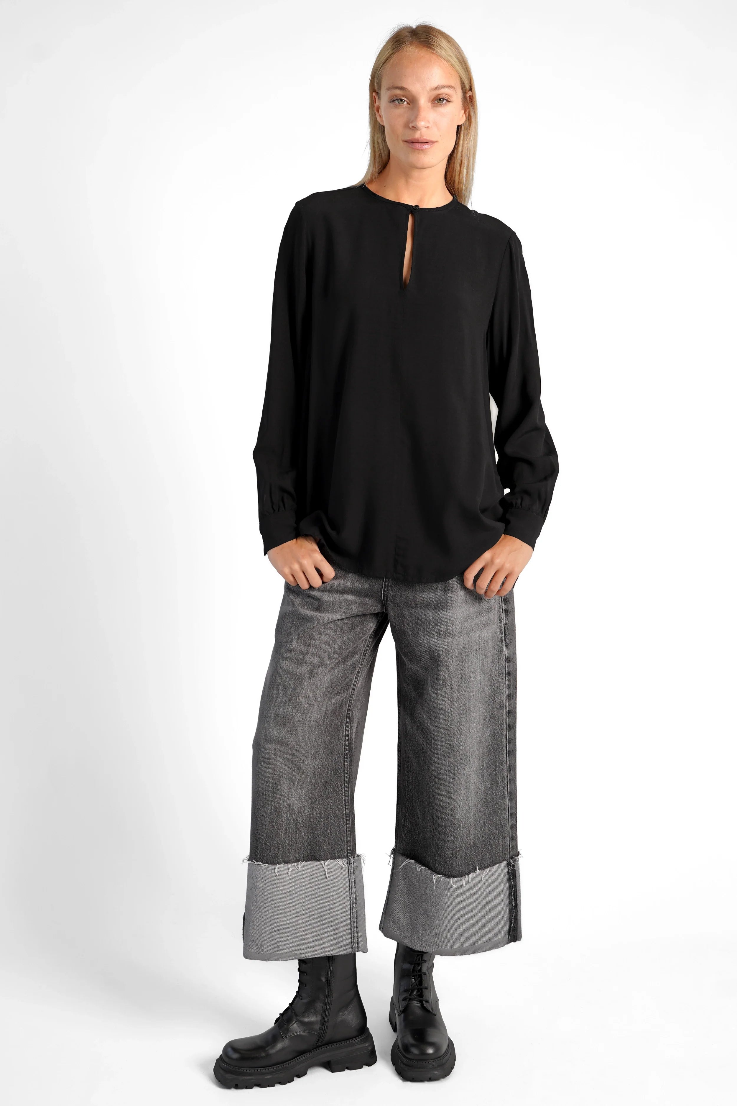 Black LYLIA.K loose fit blouse with V-neck and back pleats, worn with wide cuffed jeans and black boots.