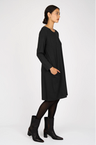 Woman wearing black A-line dress with long sleeves, side pockets, and round neckline.