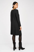 Woman wearing a black LYLLDA A-Linie Kleid dress with long sleeves, a round neckline, and a back pleat, paired with black tights and ankle boots.