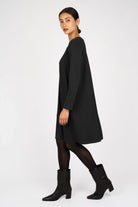 Black A-Linie Kleid with round neckline, long sleeves, and flowing A-line silhouette modeled with black tights and ankle boots.