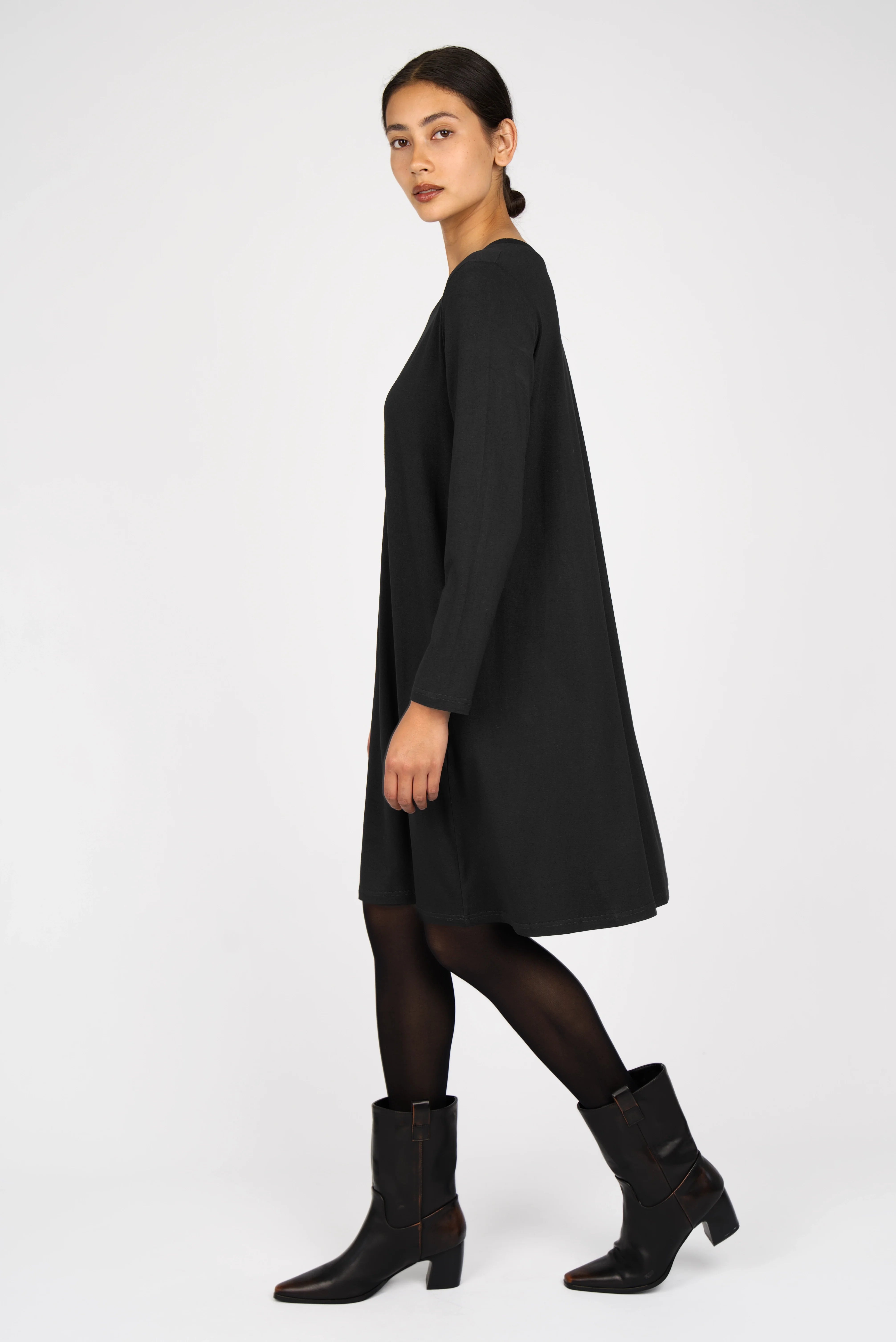 Black A-Linie Kleid with round neckline, long sleeves, and flowing A-line silhouette modeled with black tights and ankle boots.