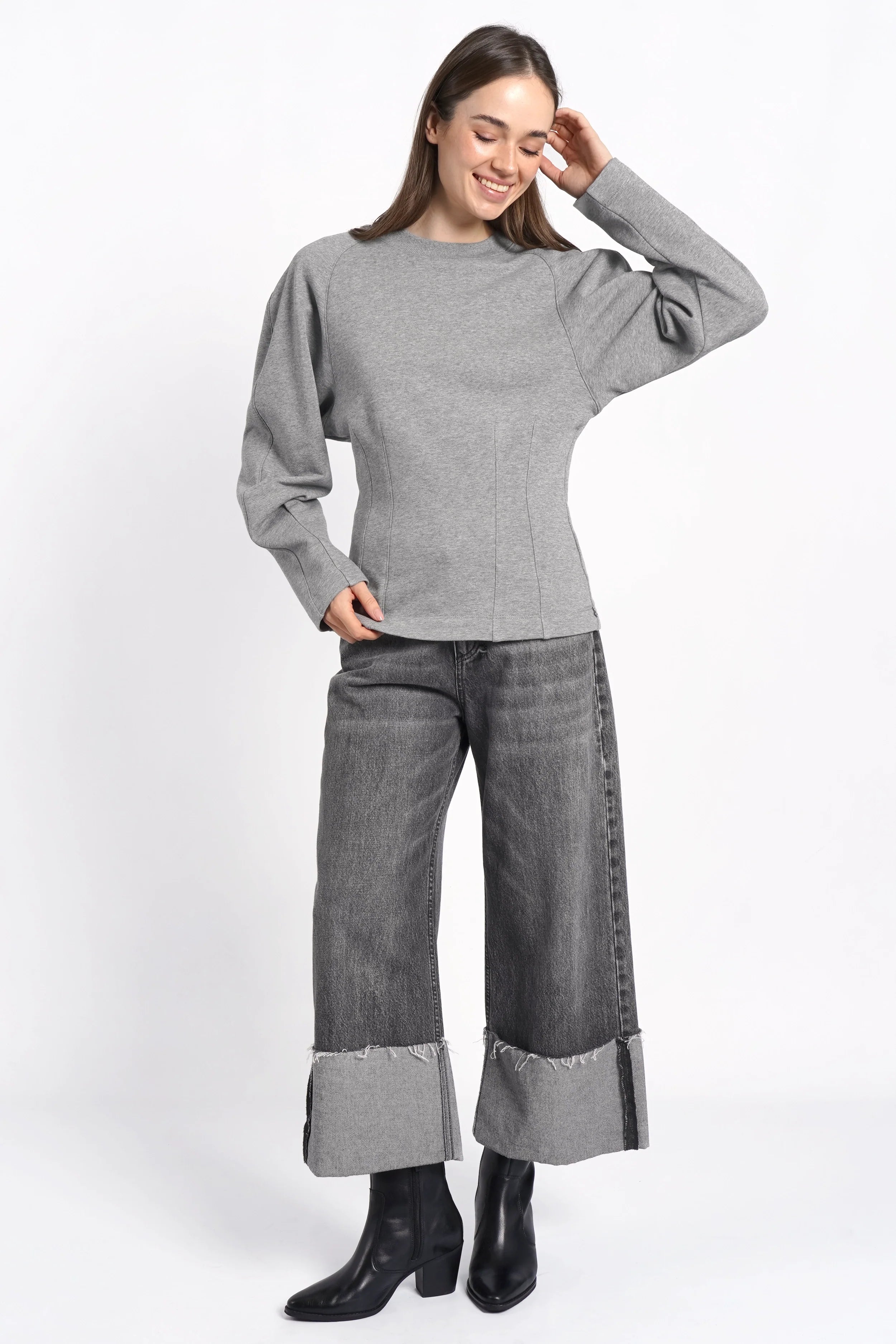 Woman wearing grey MALVEA Sweater with relaxed fit and detailed seams paired with cuffed grey jeans and black boots