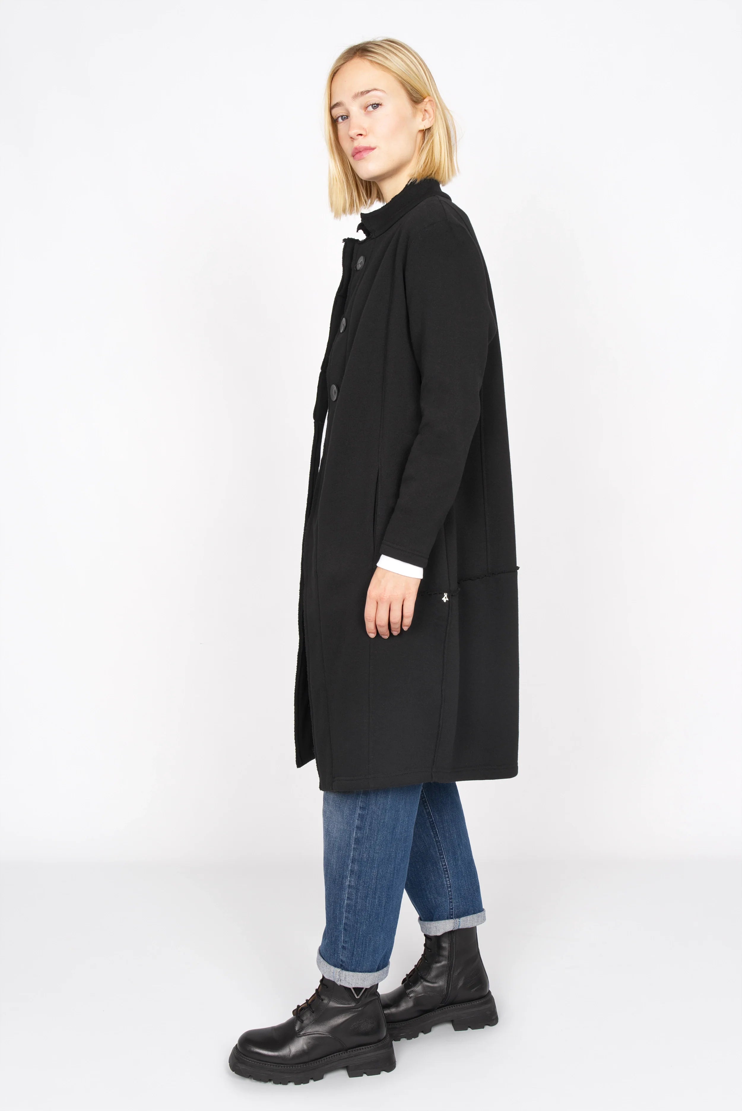Woman wearing black MANEY Sweatmantel with concealed button placket and relaxed fit standing sideways.