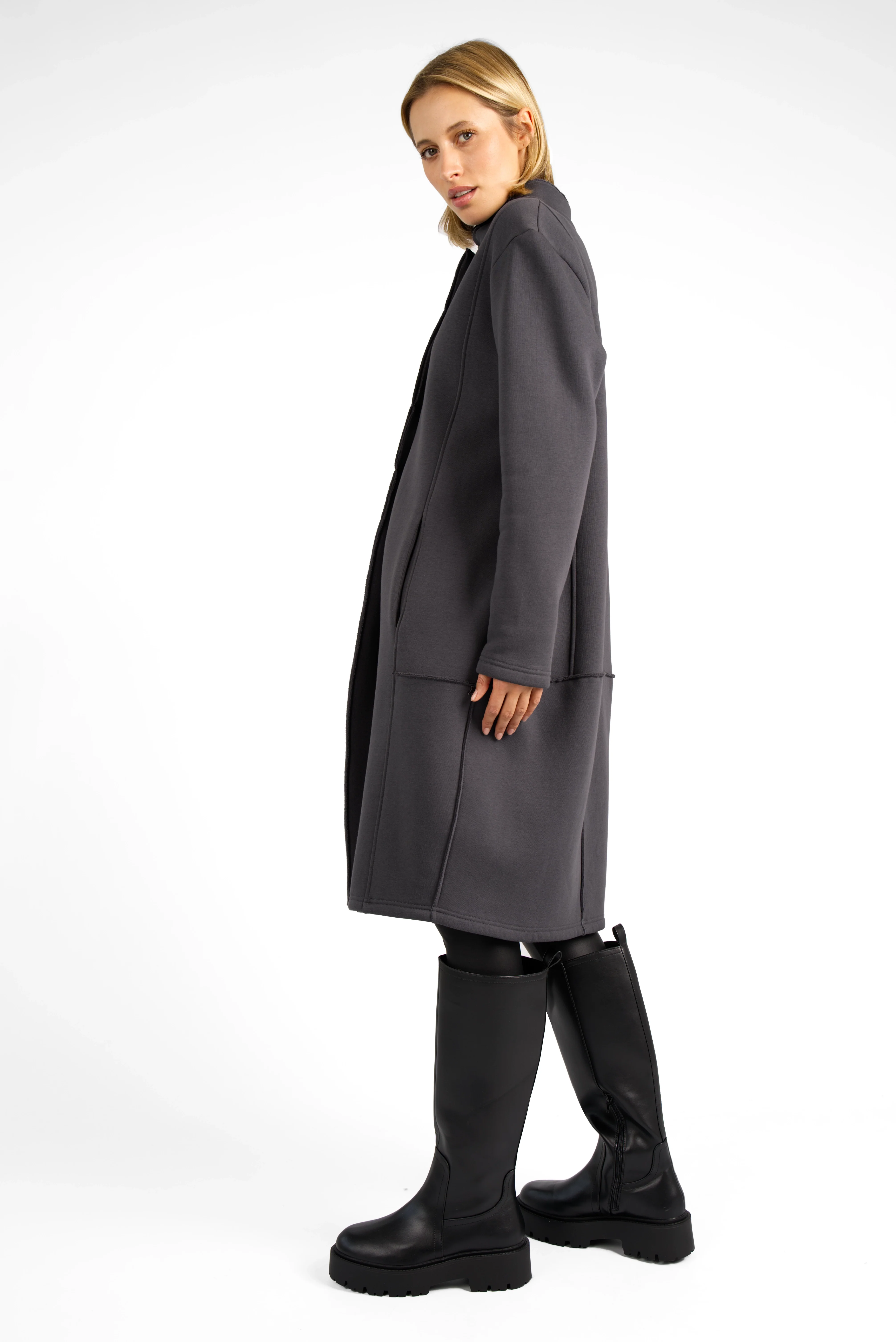 Woman wearing a dark grey MANEY Sweatmantel with concealed button placket and open-cut edges, styled with black knee-high boots.