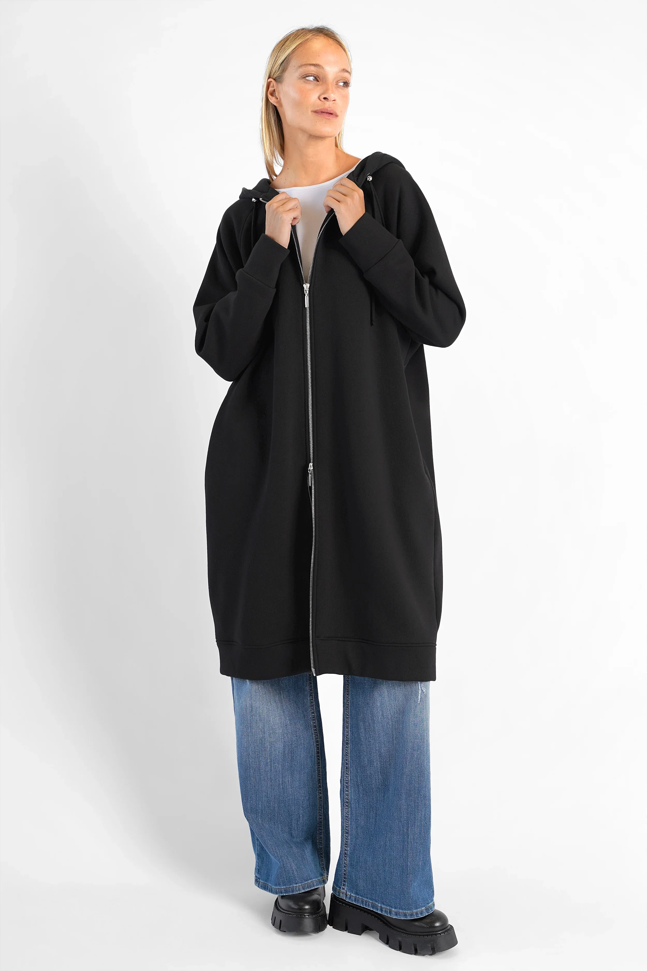 Black oversized Longzip-Hoodie with two-way zipper, hood, side pockets, and logo patch on the back worn by a female model