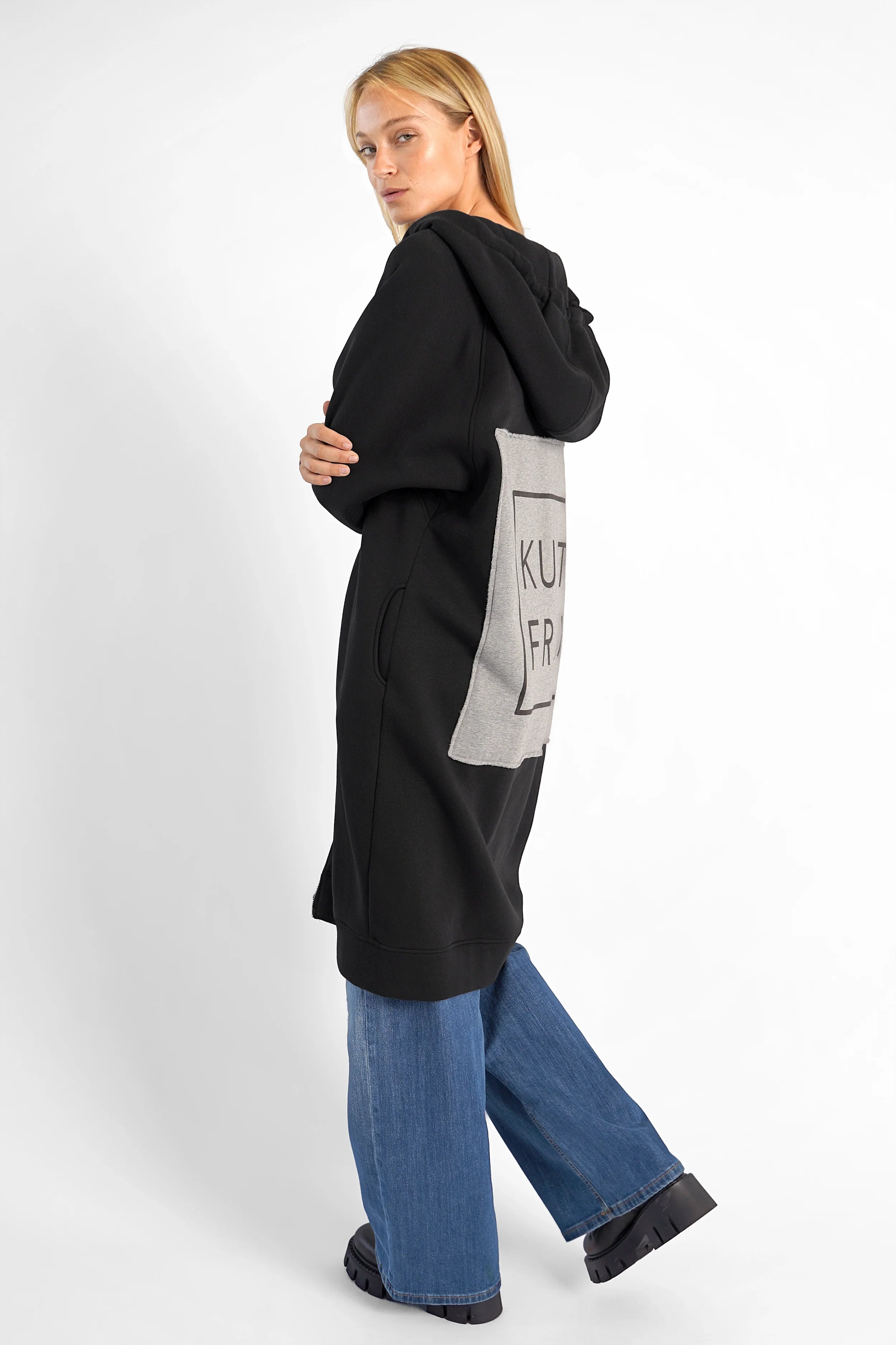 Woman wearing black MAY Longzip-Hoodie with hood and logo patch on back, paired with blue jeans