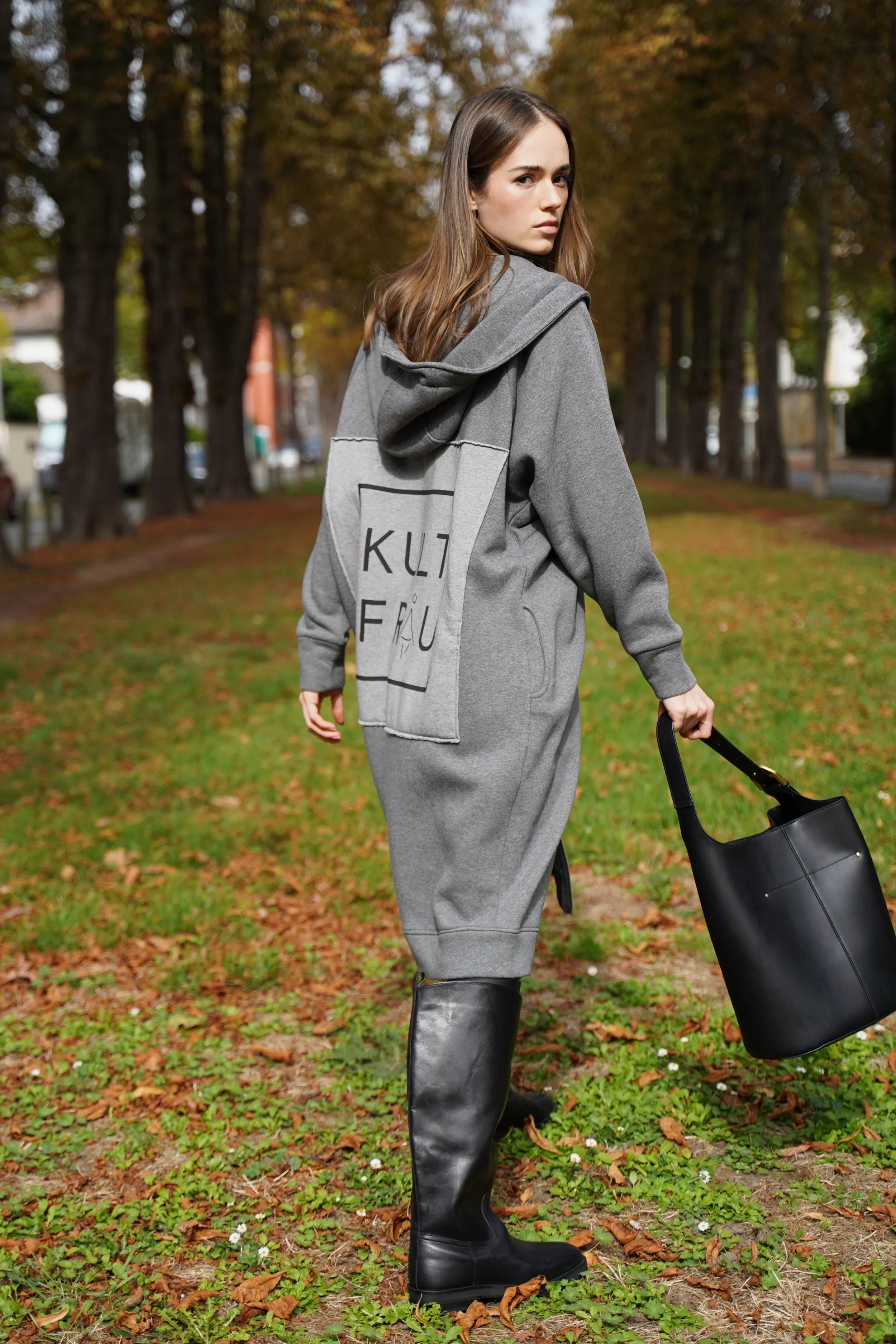 Damen grauer Longzip-Hoodie mit Kapuze, oversized Fit und aufgenähtem Logo-Patch hinten, modellgetragen im Park