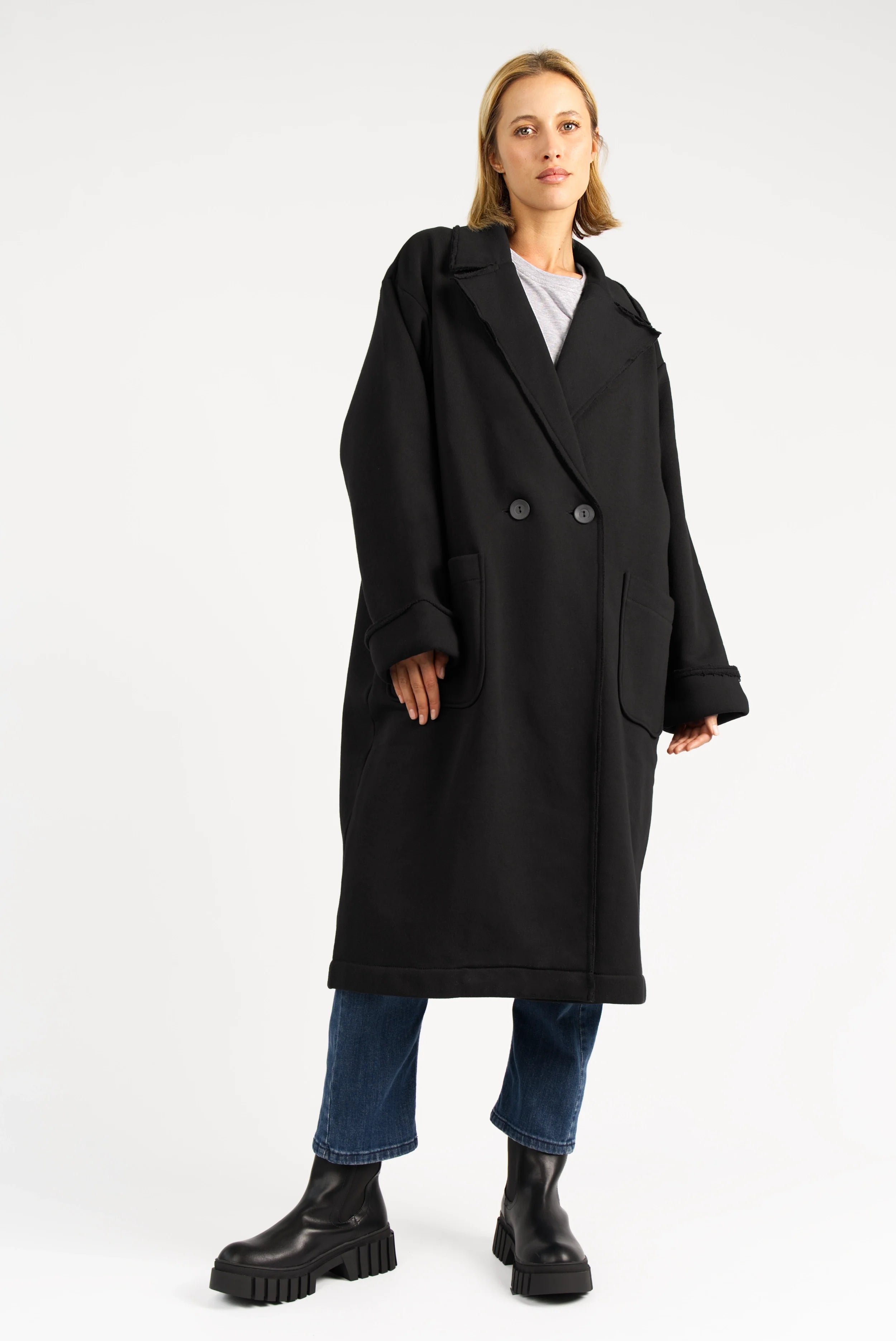 Frau trägt MONDY.K Oversize Sweatmantel aus schwarzem Jersey mit Reverskragen und großen Taschen