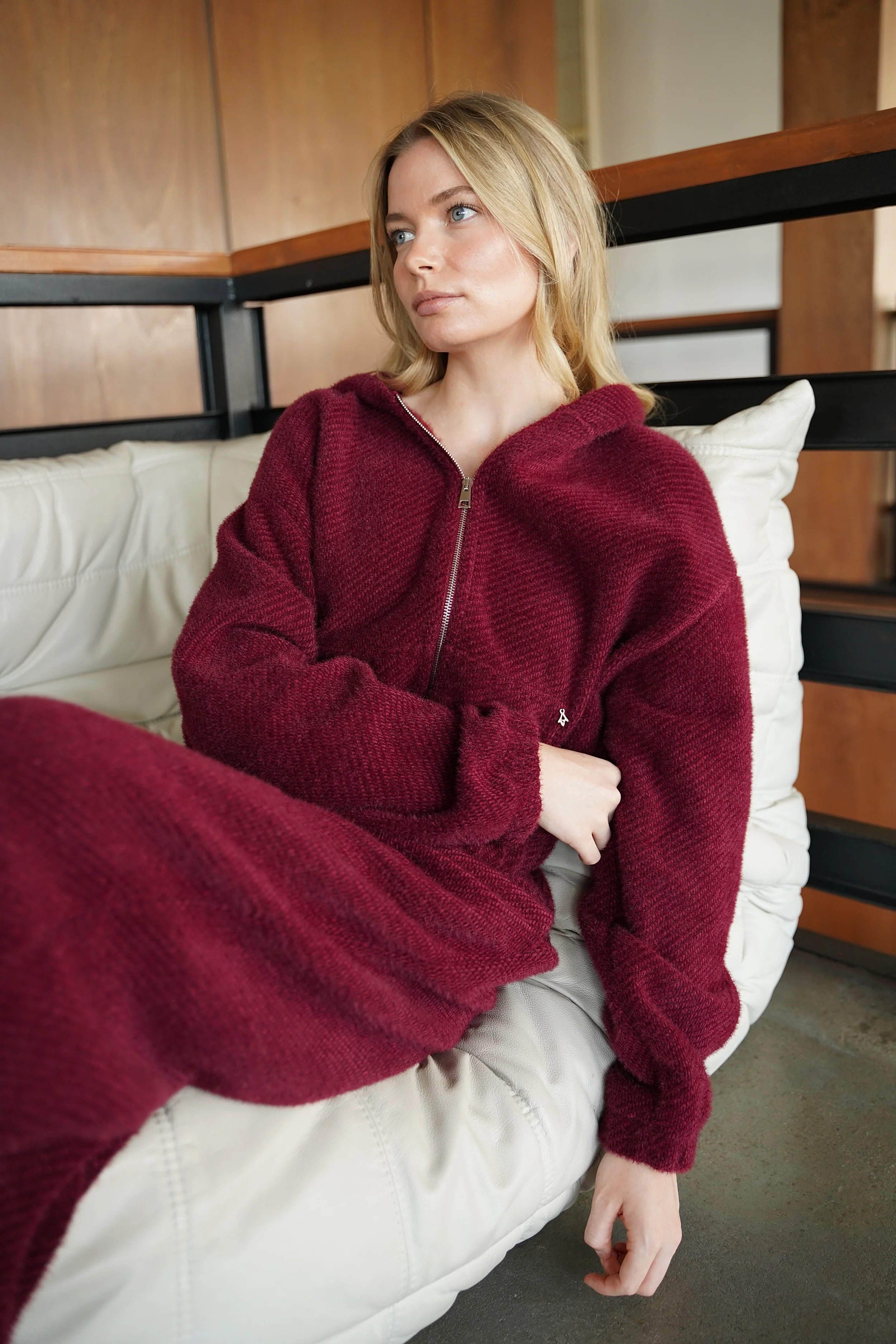 Frau trägt weichen rotbraunen Zip-Hoodie mit samtiger Kurzhaarfell-Struktur und Metallreißverschluss, entspannter Passform und geteilter Kängurutasche