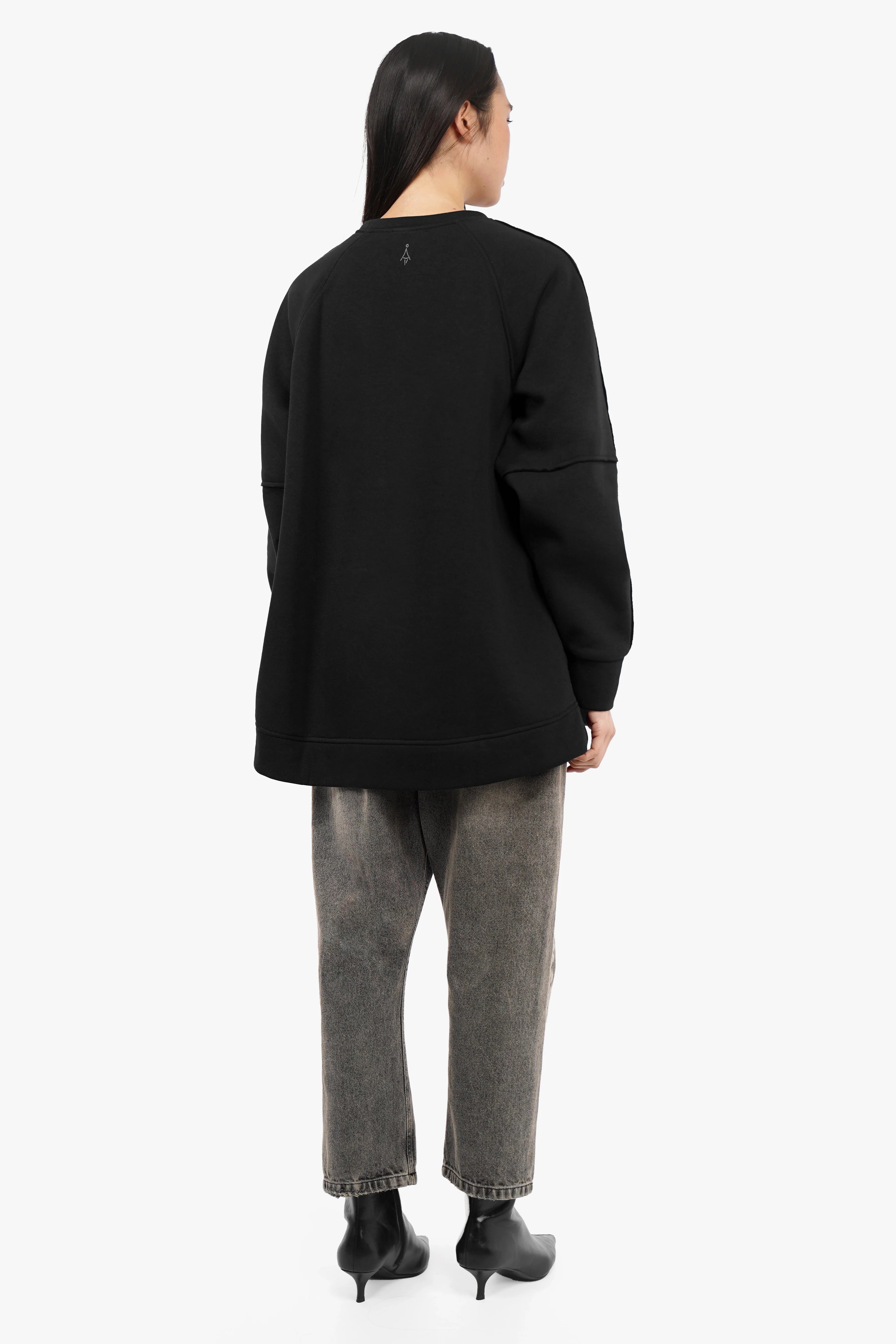 Back view of a black NAIRA Cozy Sweater with A-line silhouette, brushed soft cotton fabric, and relaxed fit worn by a model