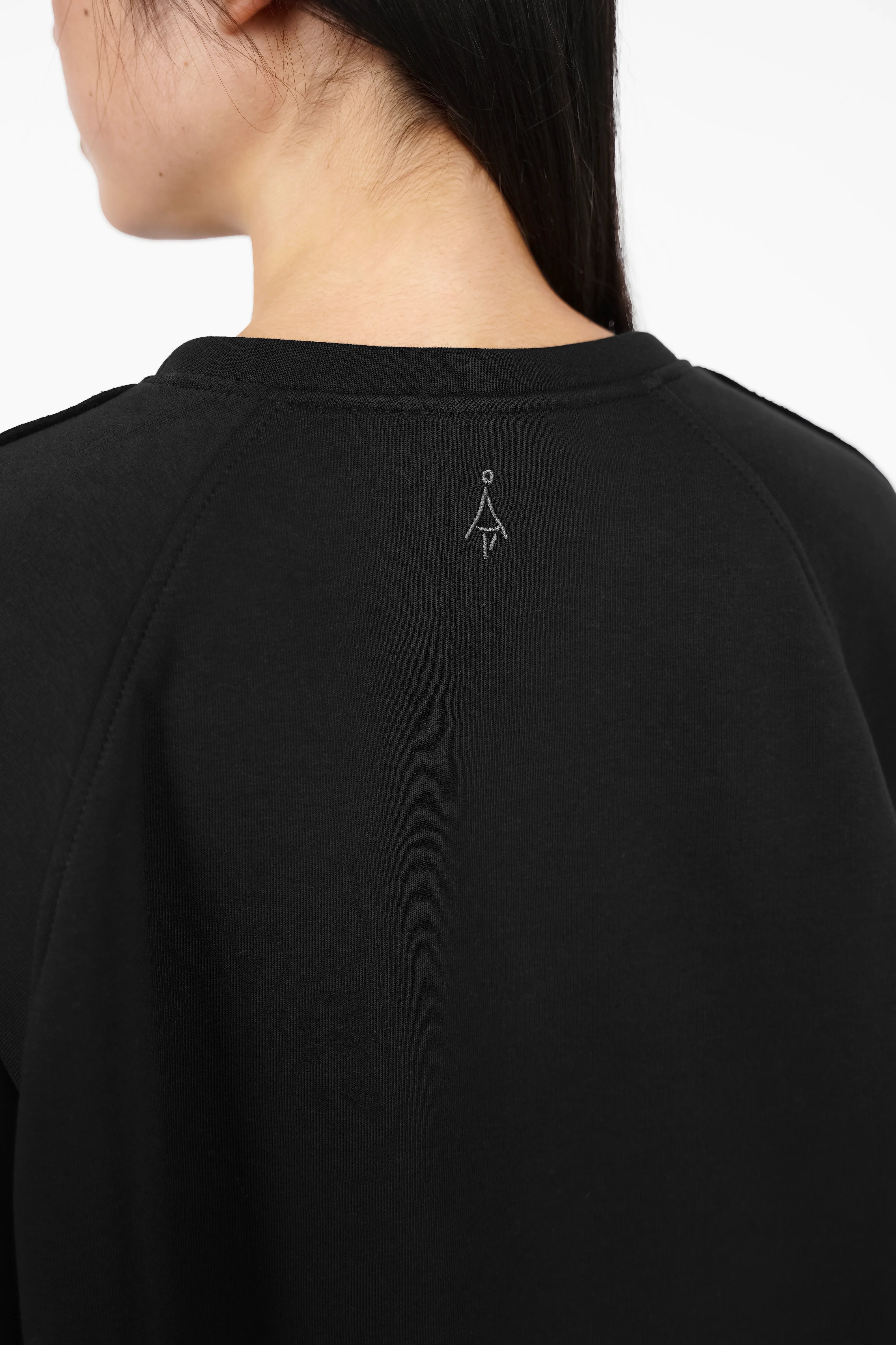 Close-up of the back of a black NAIRA Cozy Sweater showing soft cotton fabric with subtle tone-on-tone logo embroidery.