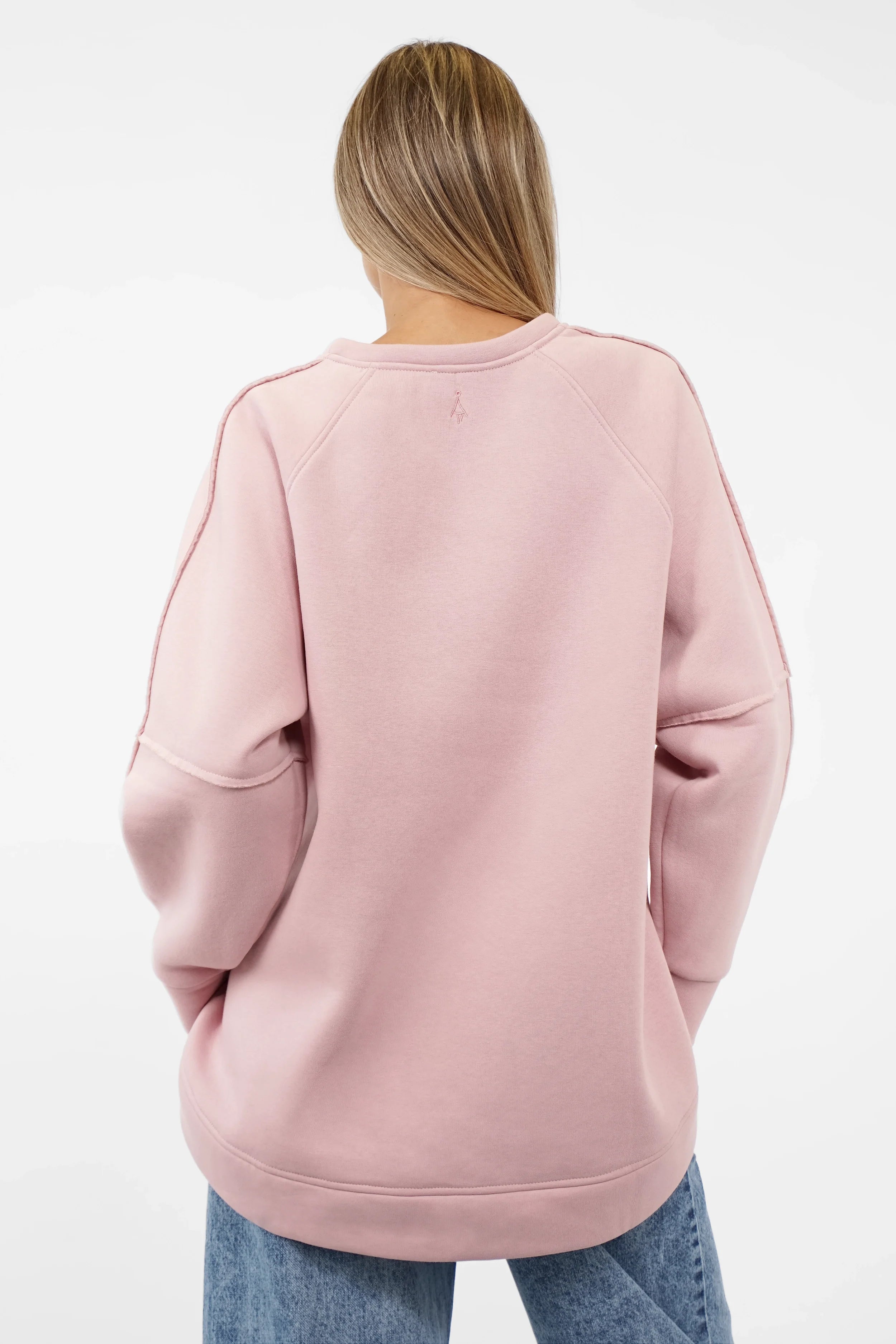 Back view of a woman wearing a soft pink NAIRA Cozy Sweater with A-line silhouette and brushed cotton interior.