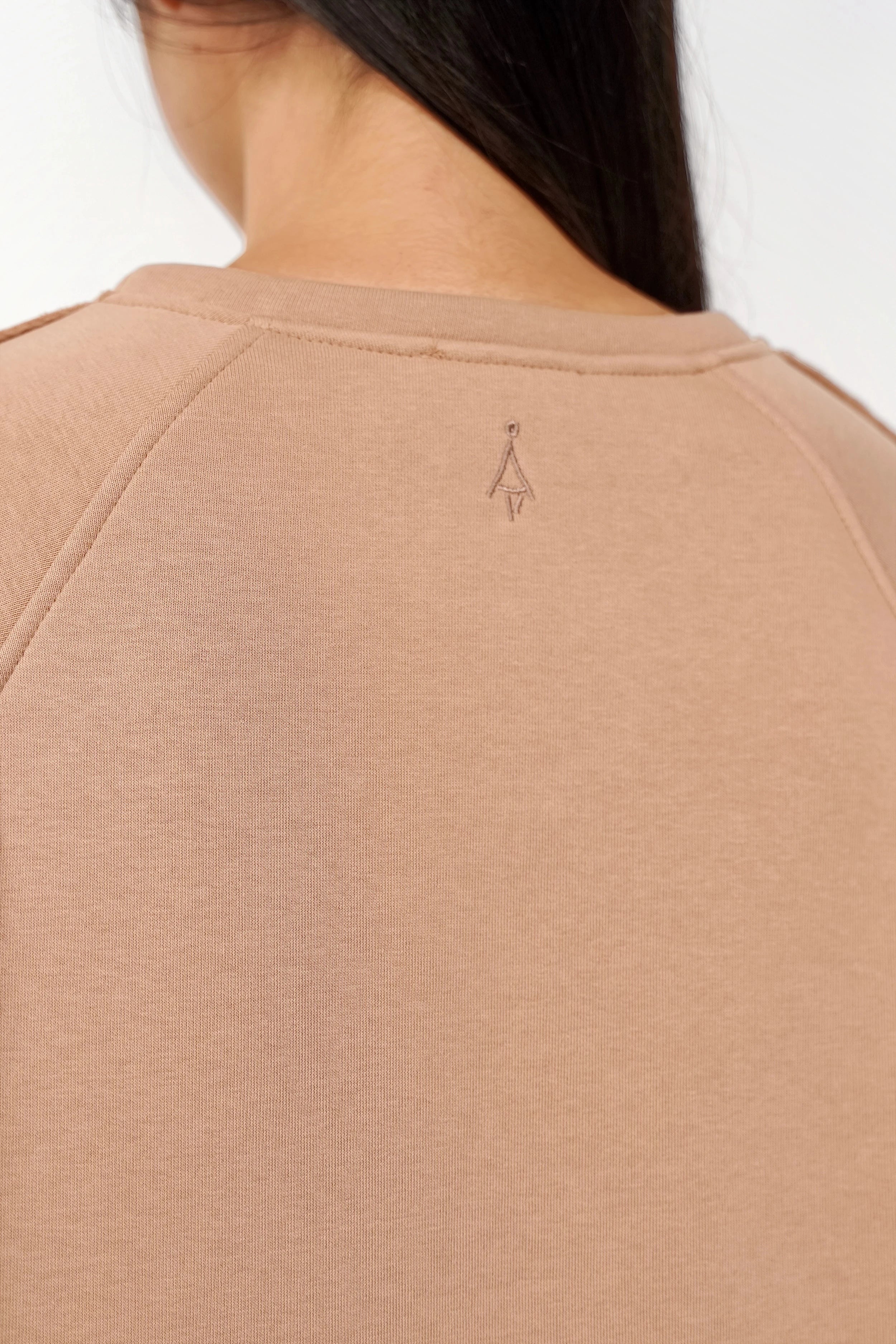 Rückenansicht des NAIRA Cozy Sweaters aus weicher, gebürsteter Baumwolle mit dezentem Ton-in-Ton Logo in Beige