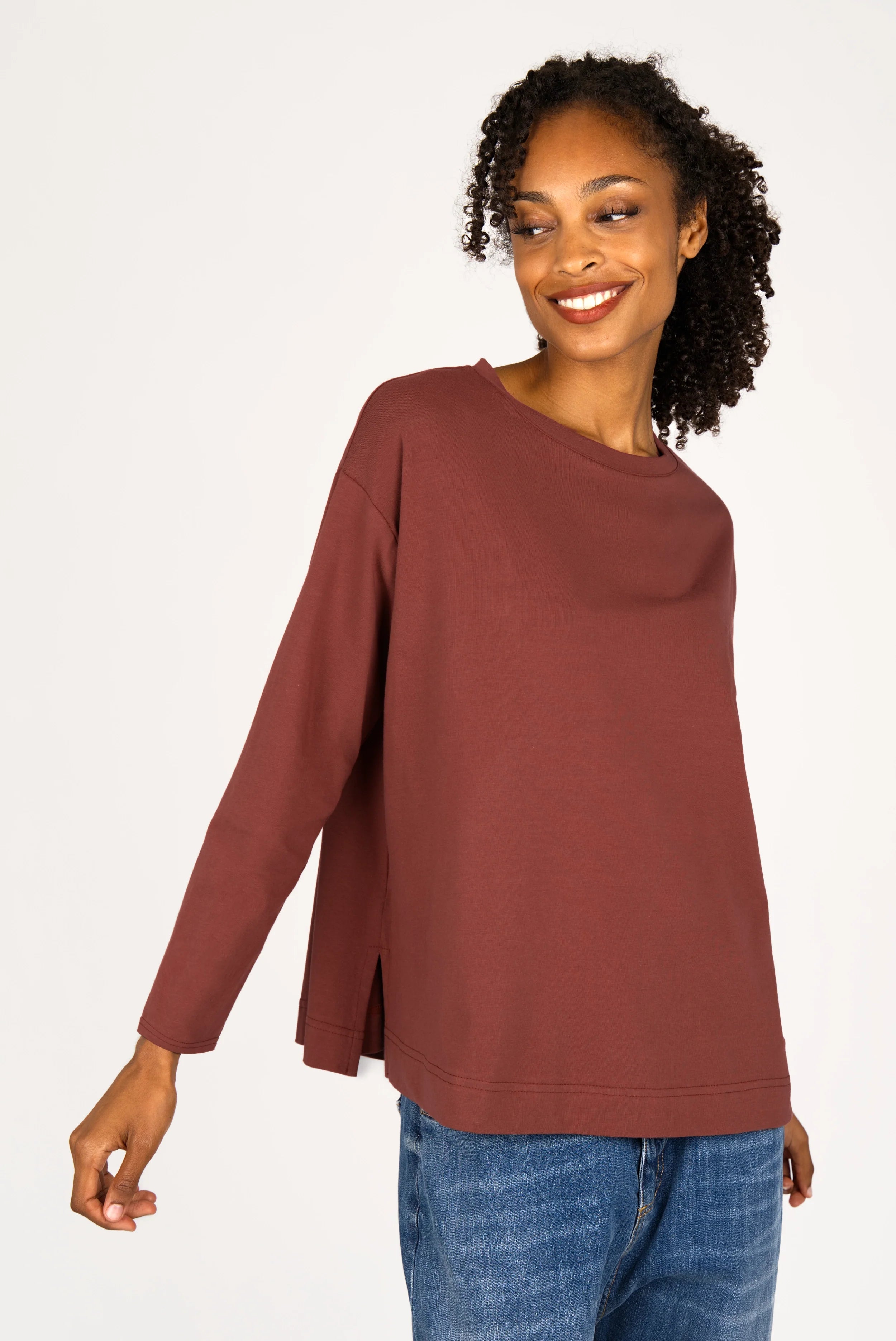 Woman wearing a relaxed fit NITI.K Langarm Shirt in brown with long sleeves, round neckline, and side slits paired with blue jeans.