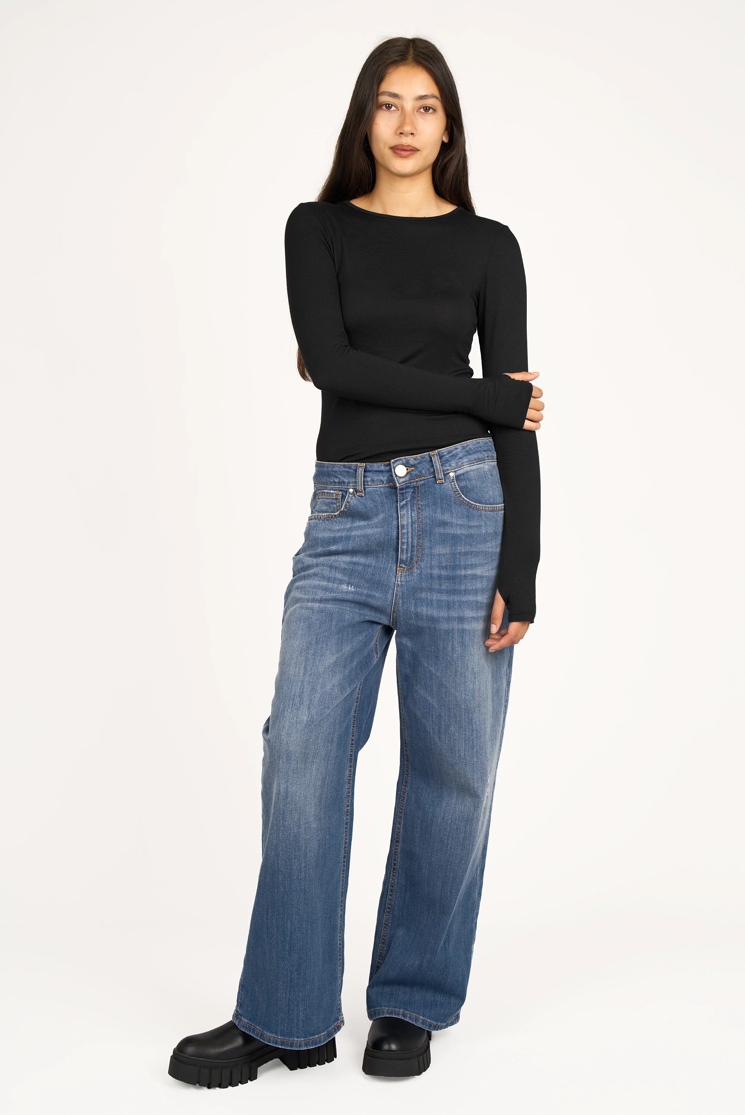 Woman wearing a black NJELI Longsleeve with round neckline, extra long sleeves with thumb holes, paired with blue wide-leg jeans