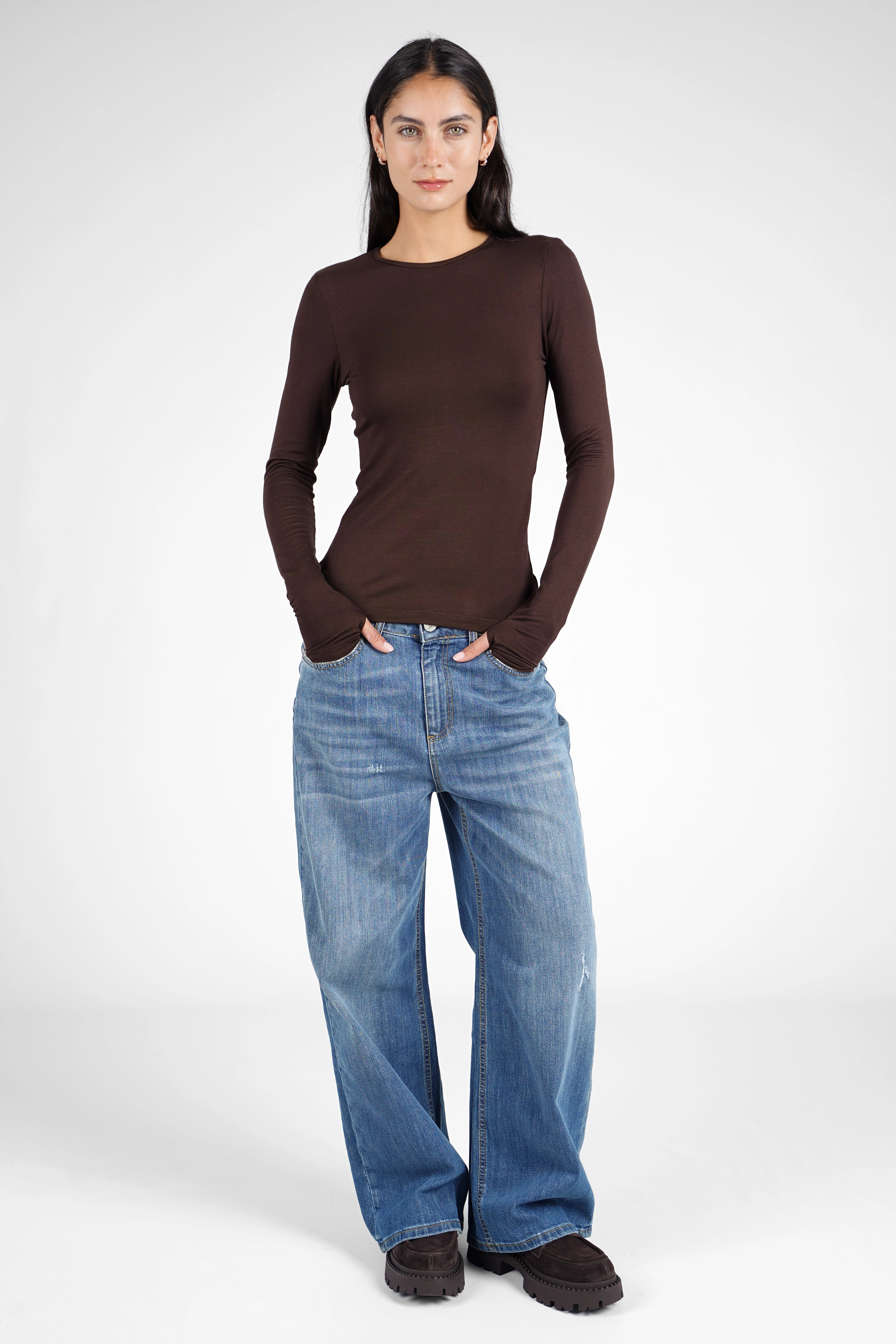 Woman wearing brown NJELI Longsleeve with round neckline, extra long sleeves with thumb holes, paired with blue wide-leg jeans