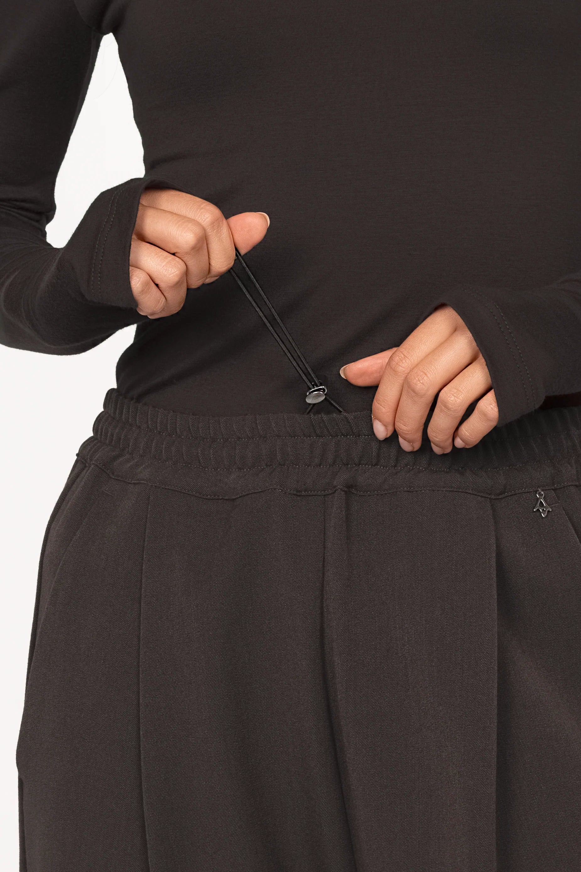 Close-up of a person adjusting the elastic waistband with stopper on the black ONAH Wide-Leg Hose featuring side pockets and subtle front pleats.