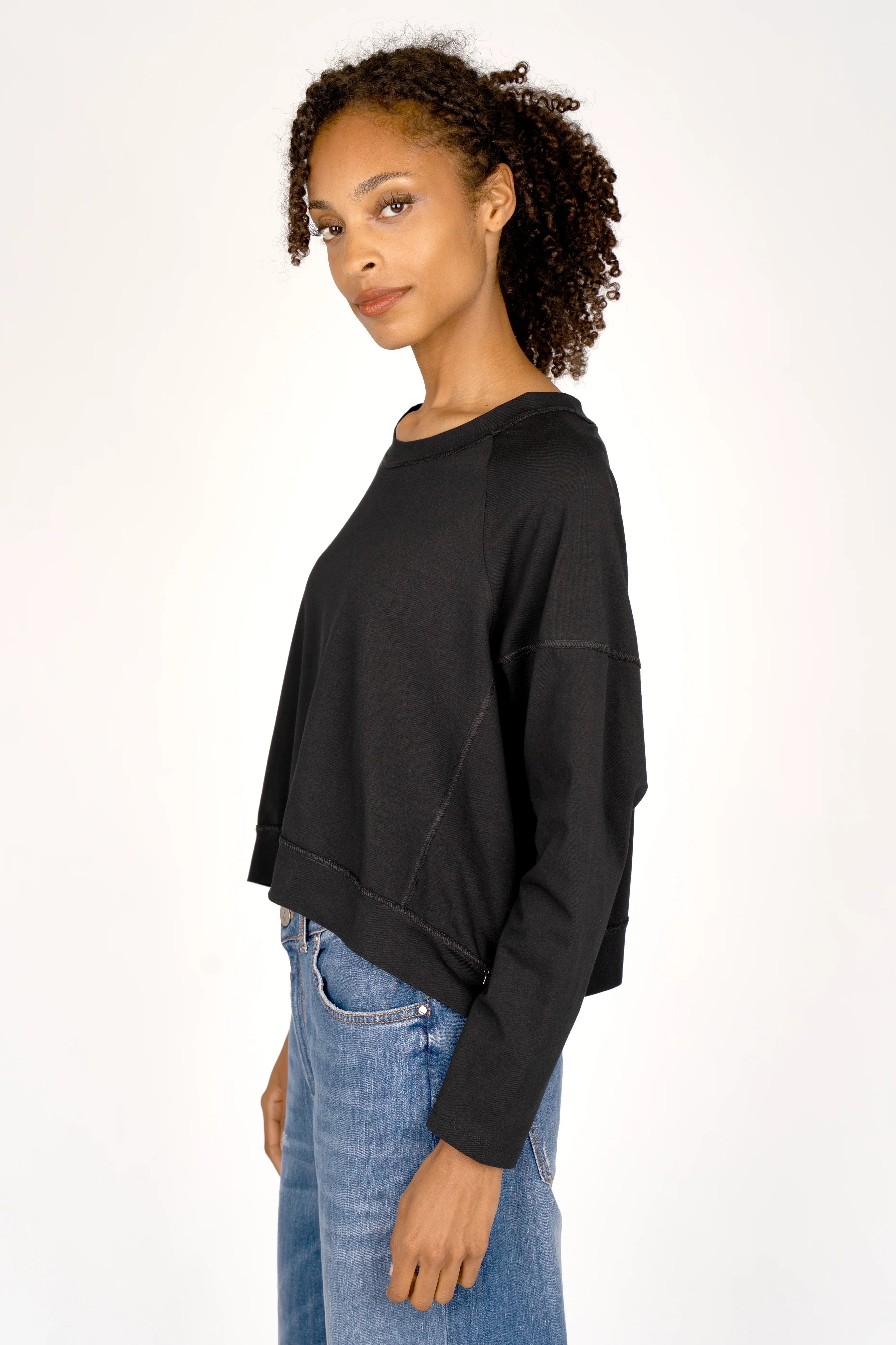Frau trägt schwarzes OSASU Cropped Longsleeve mit weitem Rundhalsausschnitt und lockerer Kastenform