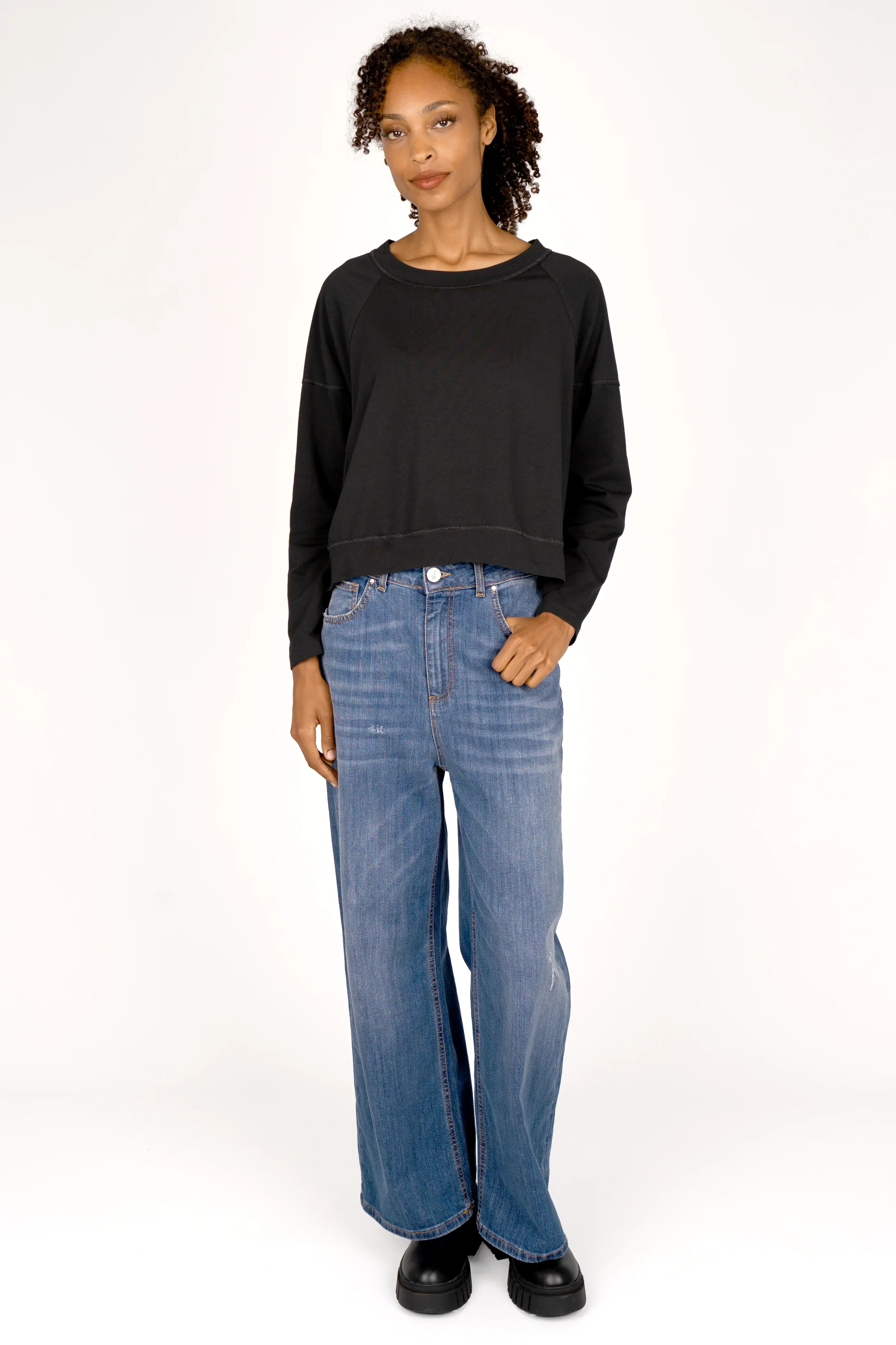 Frau trägt schwarzes OSASU Cropped Longsleeve mit weitem Rundhalsausschnitt und lockerer Kastenform zu blauen Jeans