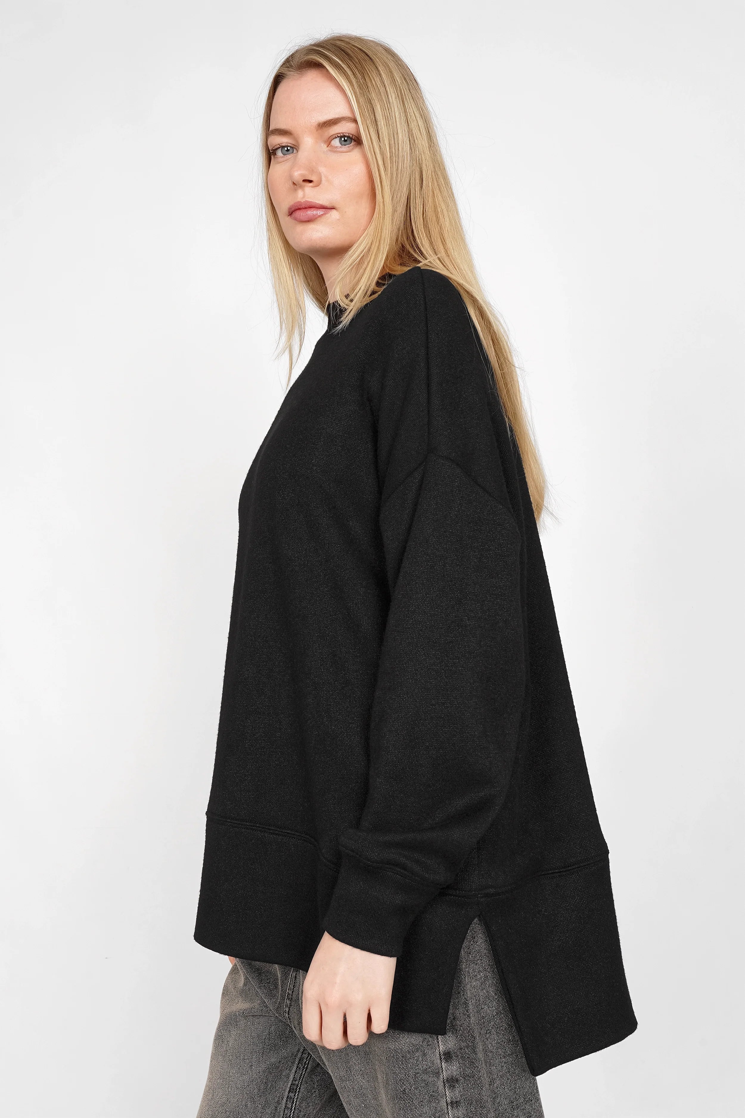 Damenmodel trägt schwarzes PATI.K Oberteil aus softem Feinstrick mit relaxed fit, überschnittenen Schultern, Rundhalsausschnitt und seitlichen Schlitzen