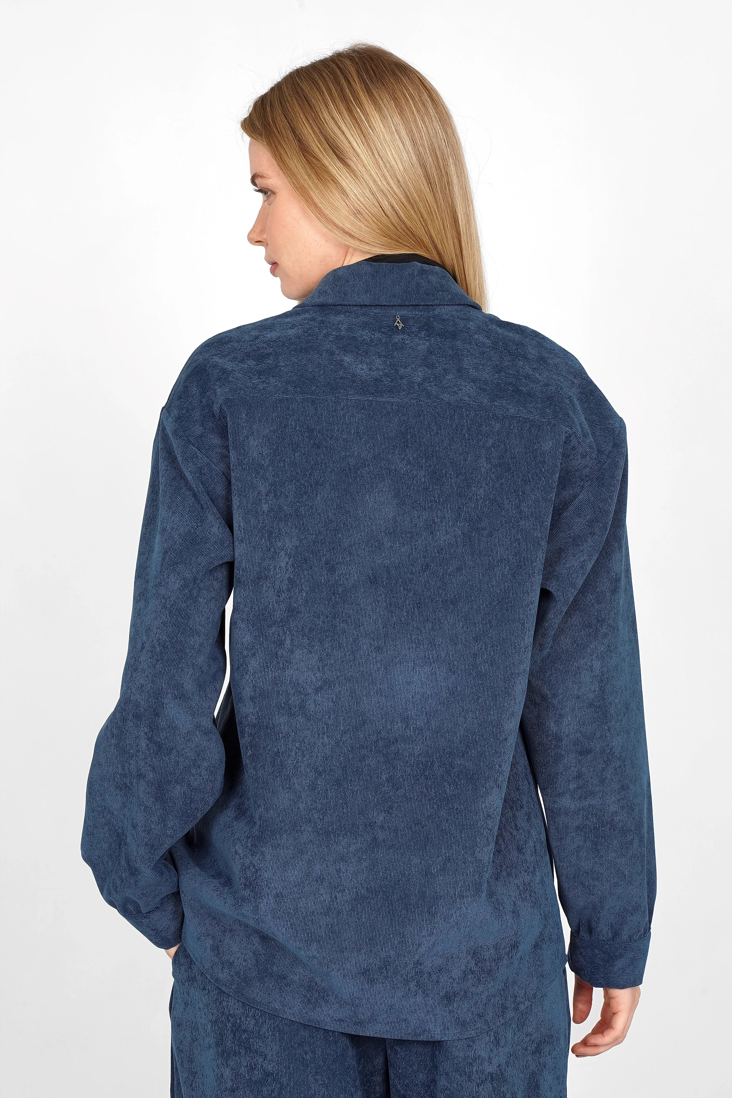 Back view of model wearing blue POULA Cord Overshirt with relaxed fit and soft texture